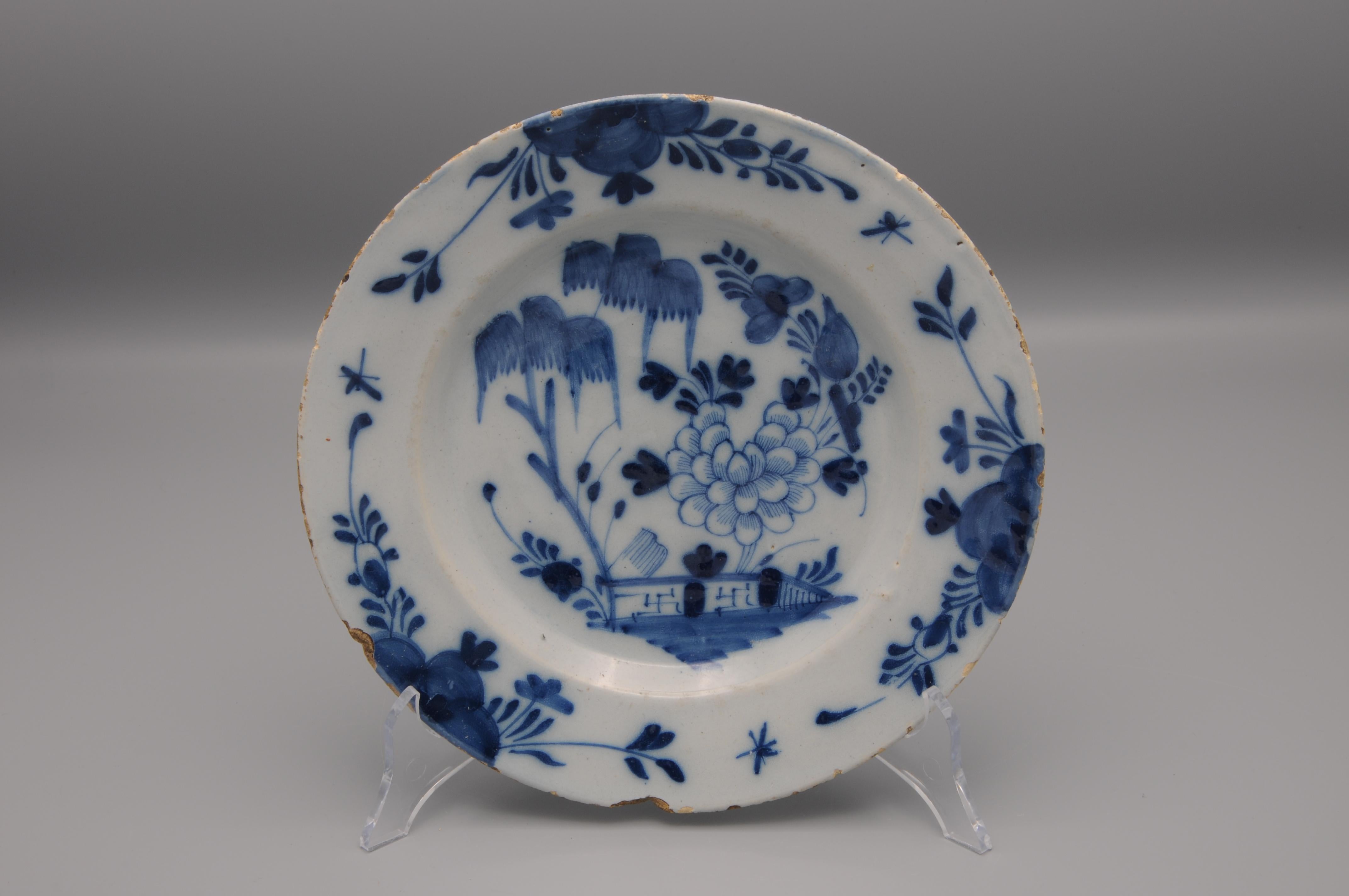 Dutch Delft blue and white plate with a 'Chinoiserie' decoration of a landscape with a fence, flowering peony and willows. 

Good condition: light chipping and some usual wear to the rim. Chip on the lower section of the rim. 