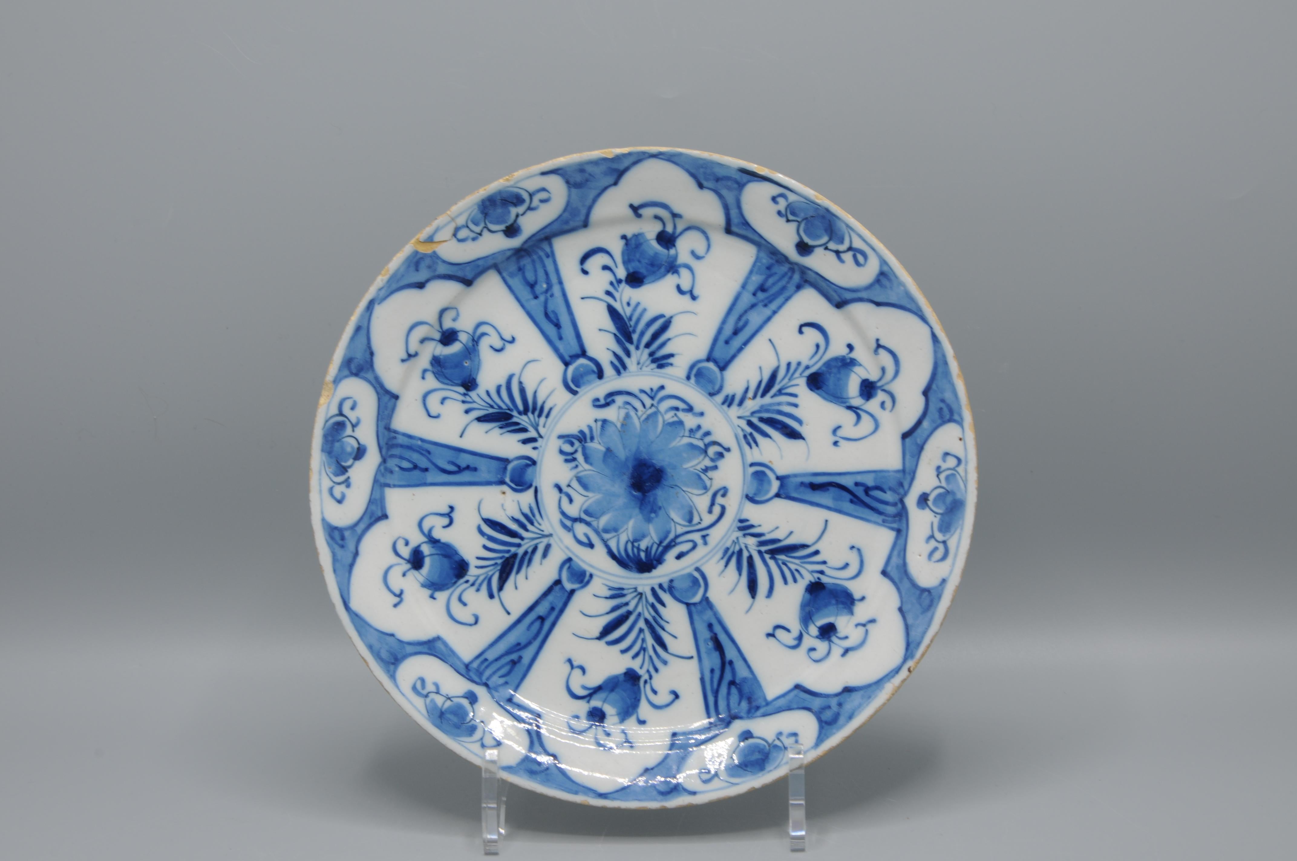 Delfter Fayence-Teller mit geometrischem Chinoiserie-Dekor
Auffälliger blau-weißer Delfter Porzellanteller mit einem zentralen Medaillon mit stilisiertem Blumenmotiv. Die breite Bordüre ist fein verziert mit abwechselnd angeordneten Paneelen mit