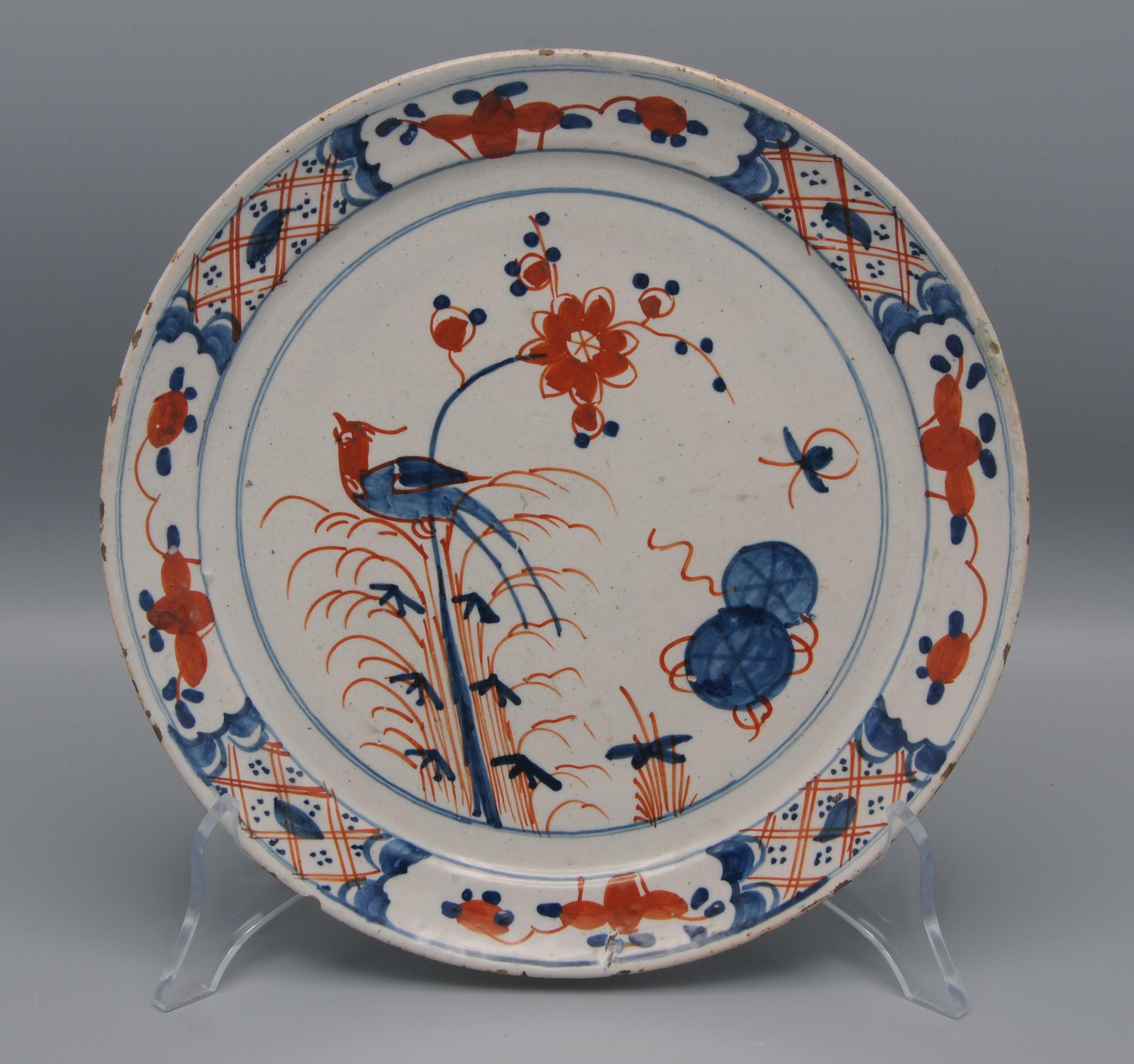 Polychrome Dutch Delft Chinoiserie plate depicting a oriental bird on a blossoming branch. 
Beautiful alternating paneling on the rim with tracery and foliage scrolls. 

Good condition: usual wear and one retouched chip to the rim.