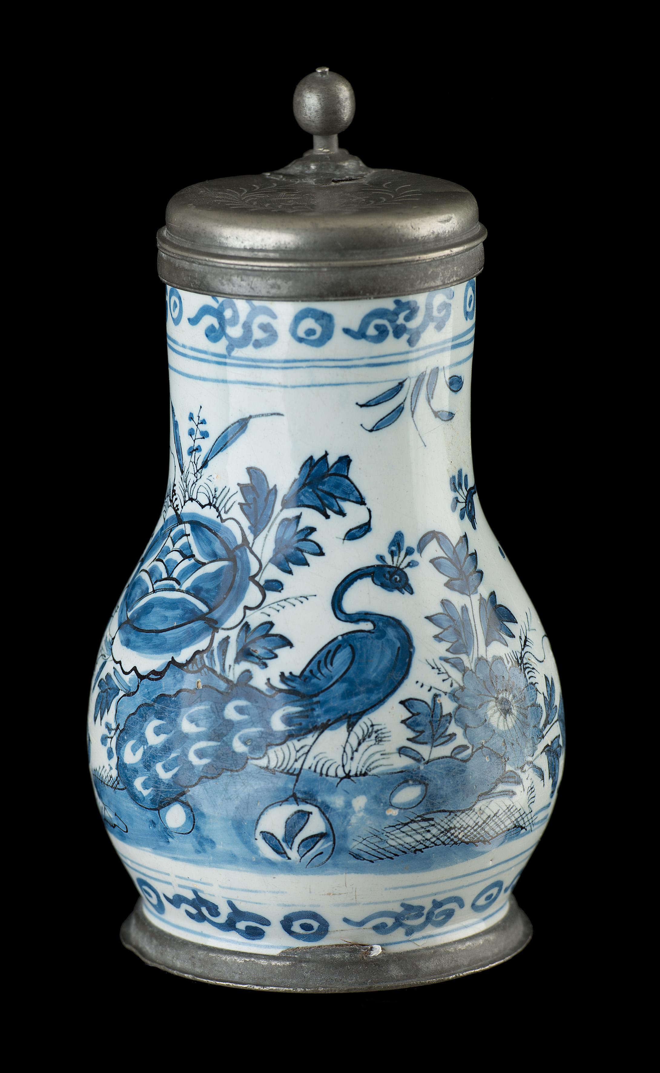 Blue and white beer mug with peacock in garden
Delft, 1680-1700 

The pear-shaped beer mug with pewter lid stands on a short foot and has an ear-shaped handle that ends in a rat tail. It is painted in blue with a continuous landscape with plants,