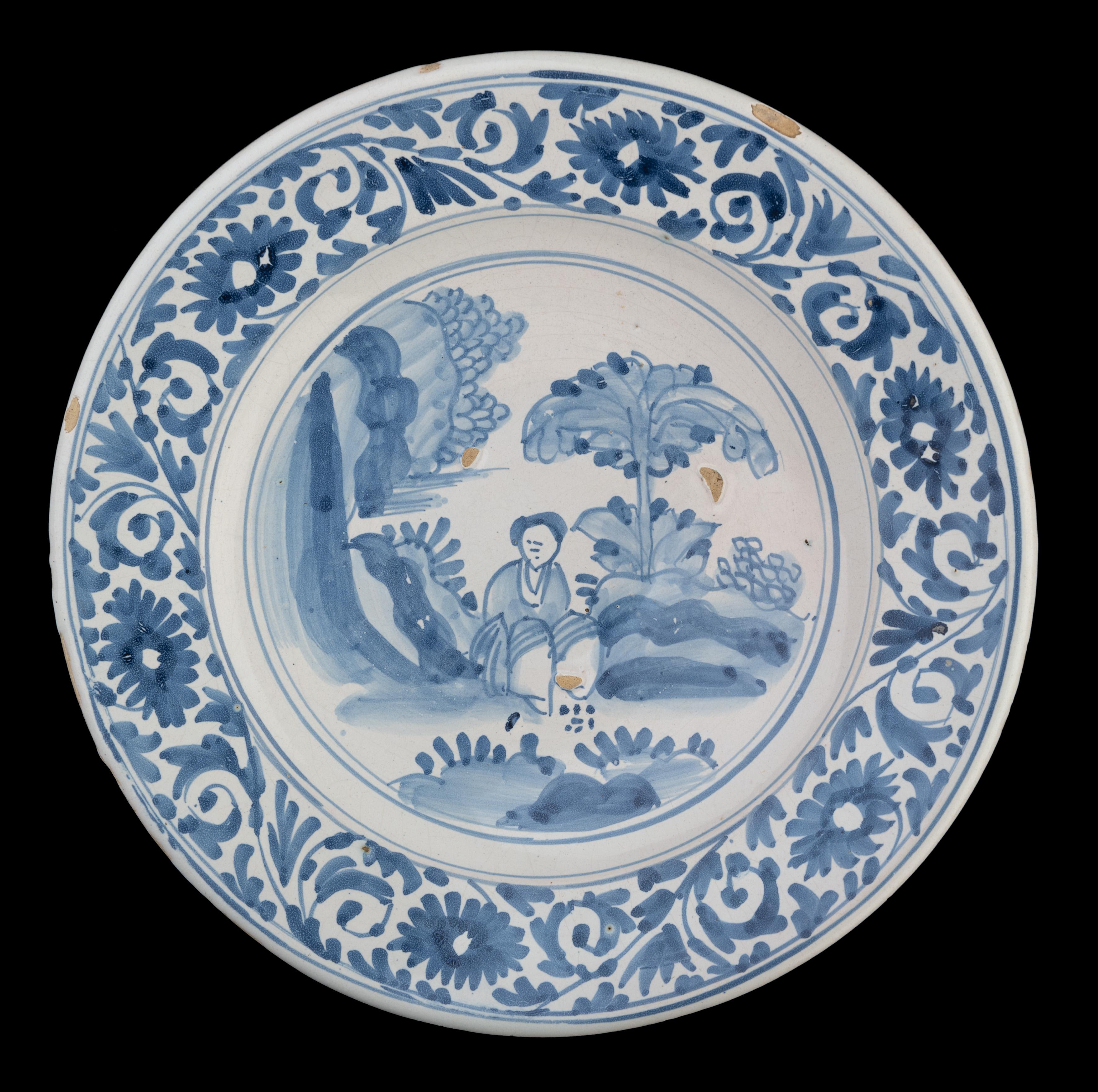 Large blue and white chinoiserie dish. The Netherlands, 1675-1700.

The blue and white dish has a wide-spreading flange and is painted in the centre with a sitting Chinese figure in an oriental landscape, within a double circle. The well is left