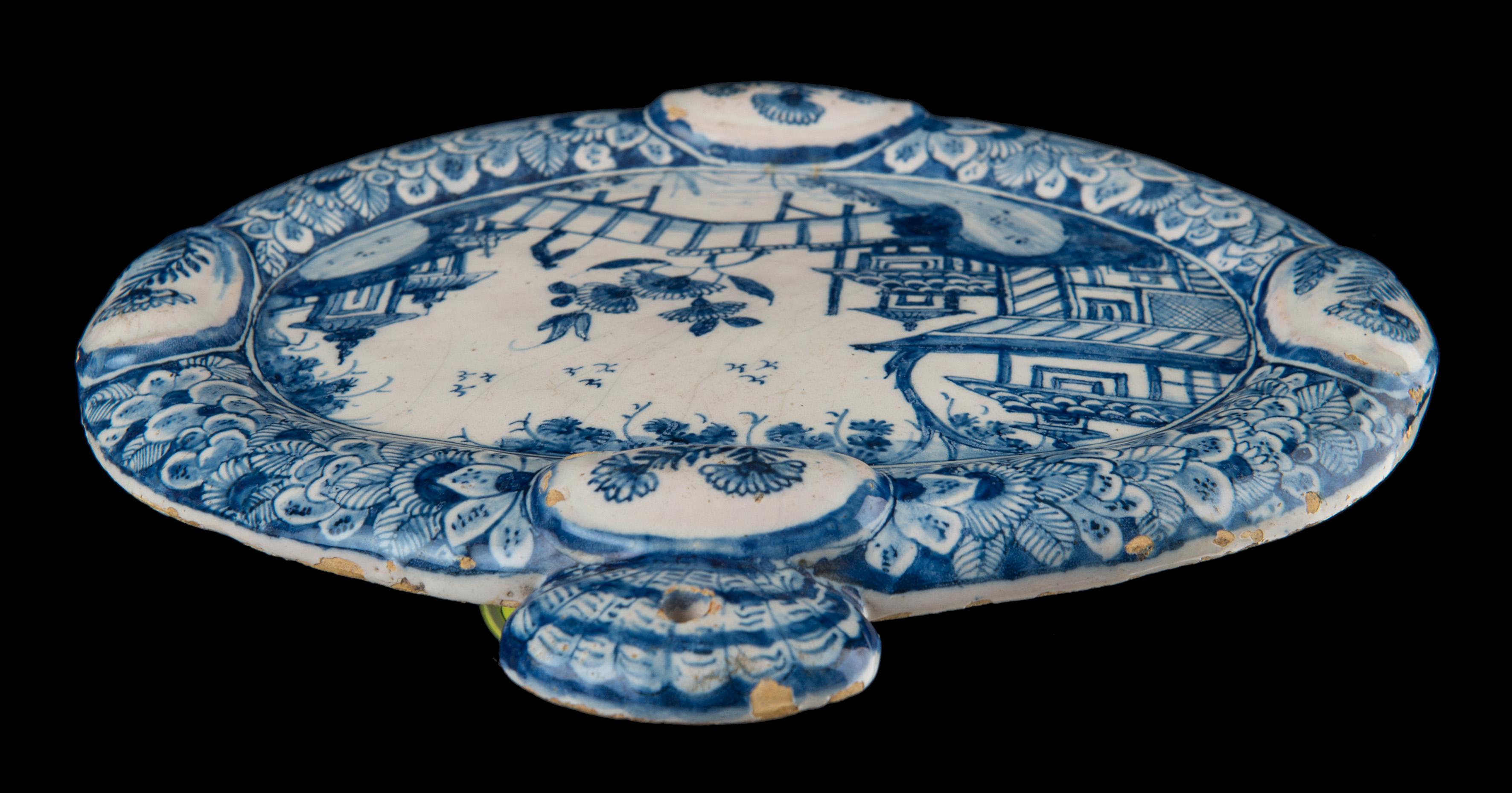 Blue and white chinoiserie plaque. Delft, 1740-1760

The oval blue and white plaque has a molded rim with four raised, oval cartouches. At the top a shell-shaped suspension loophole is molded. The plaque is painted with a chinoiserie water