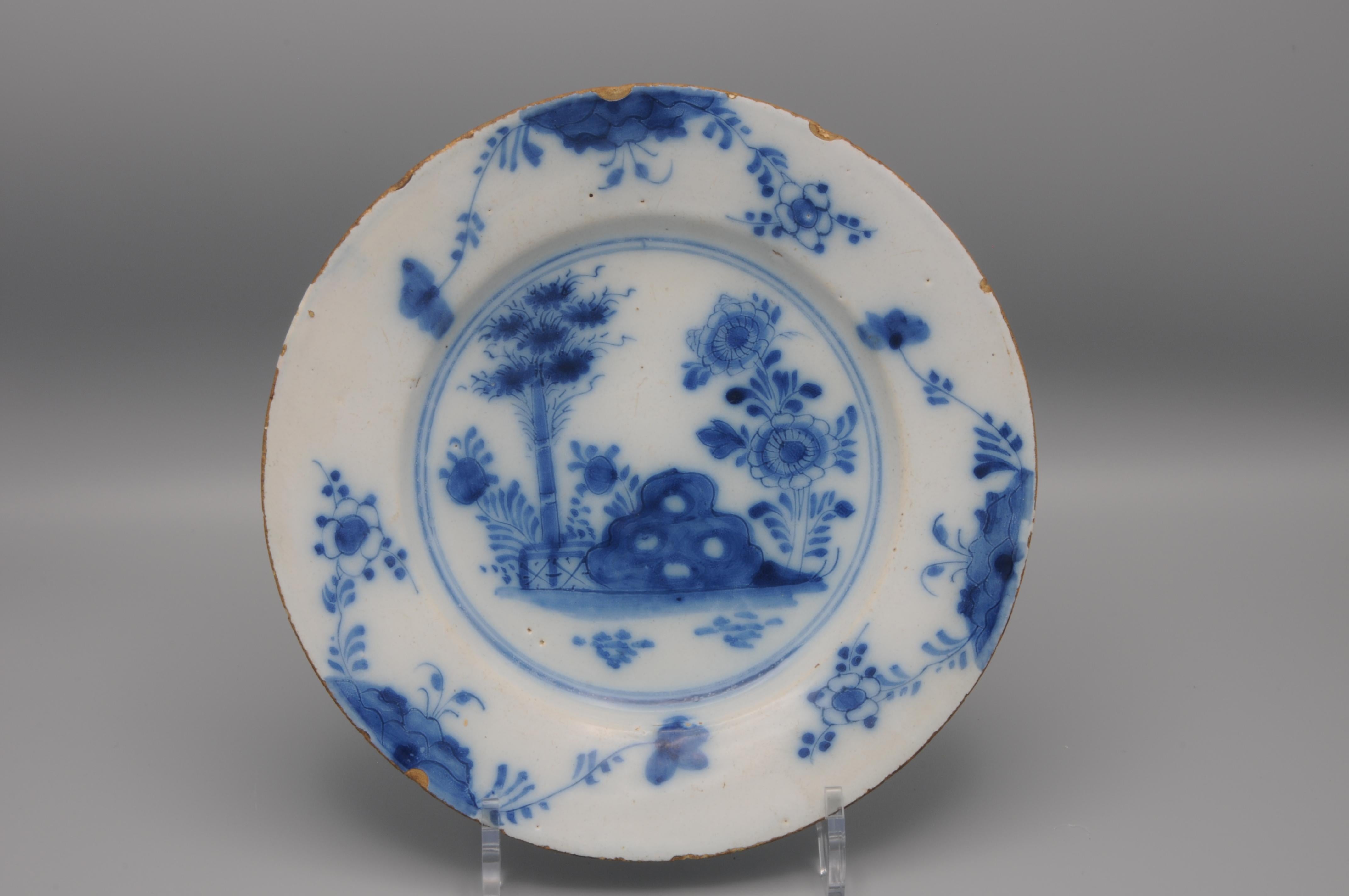 Assiette de chinoiserie bleue de Delft représentant un massif d'arbustes et une pivoine en fleurs derrière une clôture. Les bordures sont ornées de 3 brins de fleurs. 


Condit : quelques rayures et usures. Quelques ébréchures sur le bord. 