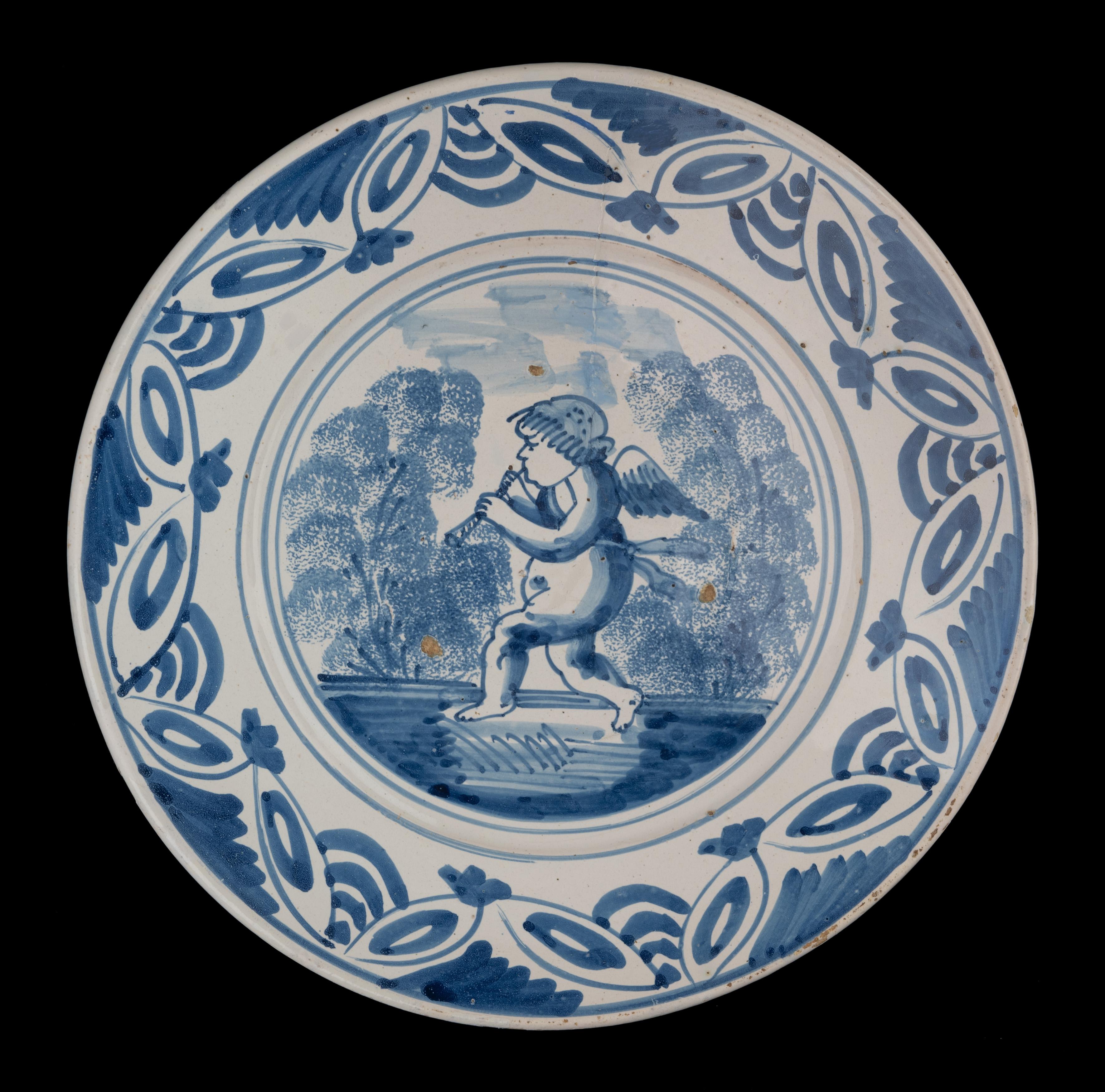 Blaue und weiße Schale mit einem Putto. Die Niederlande, 1660-1700 

Die blau-weiße Schale hat einen breiten, ausladenden Flansch und ist in der Mitte mit einem gehenden, Flöte spielenden Putto in einer vereinfachten Landschaft in einem