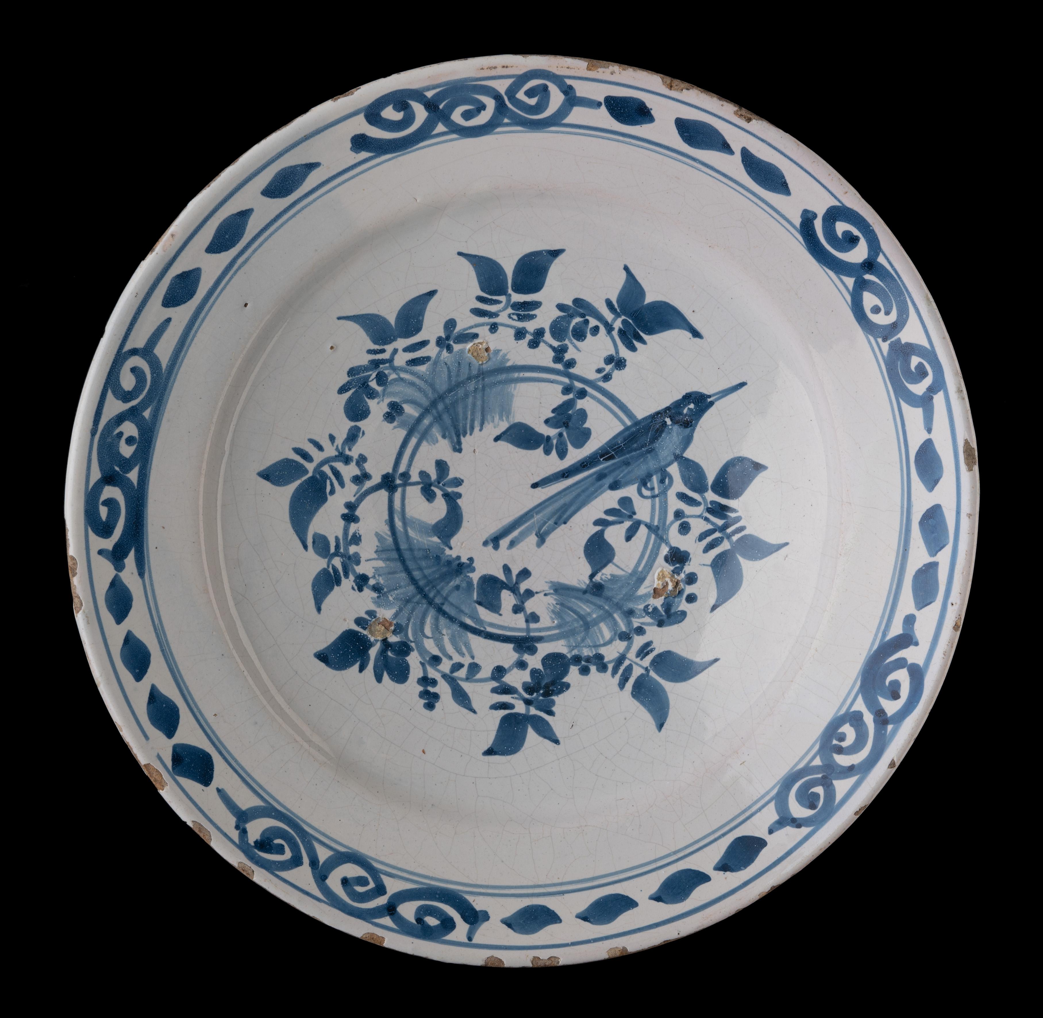 Blue and white dish with bird on a double ring
Delft or Western-Netherlands, 1700-1750 

Blue and white dish with a wide-spreading flange, painted in the centre with a bird on a double ring with leafy garlands. The decor on the flange is made up