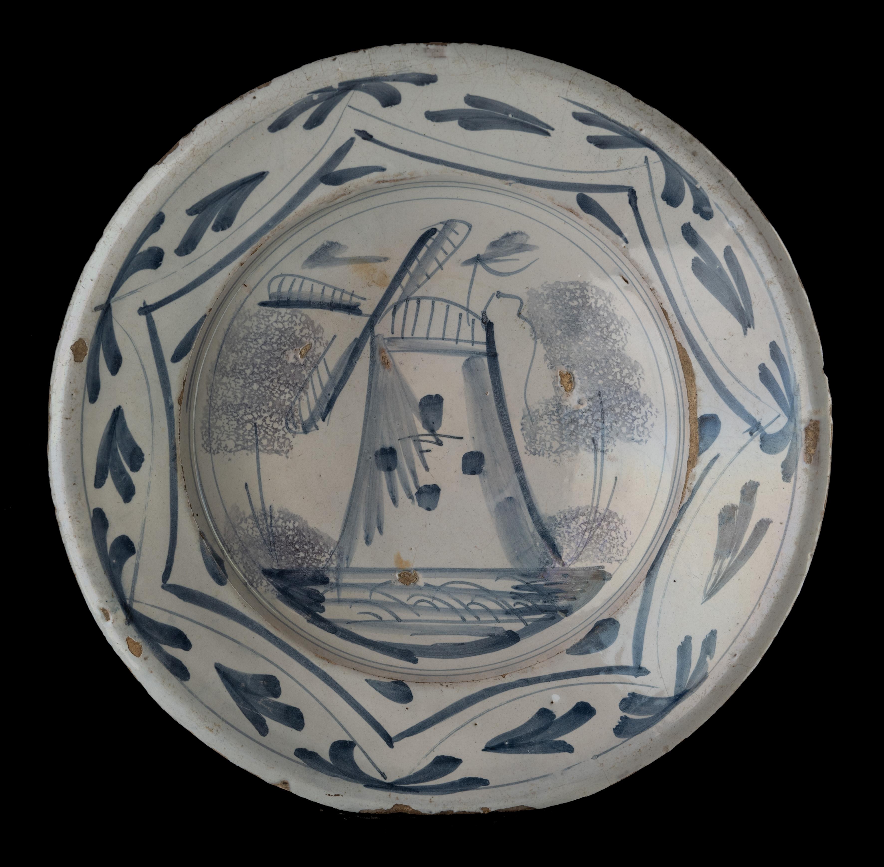 Blue and white dish with windmill.
Delft, 1700-1750 

The dish has a raised flange and is painted in blue with a windmill between two sponged trees. The depiction is framed within three circles. The border decor is made up of a heptagon with