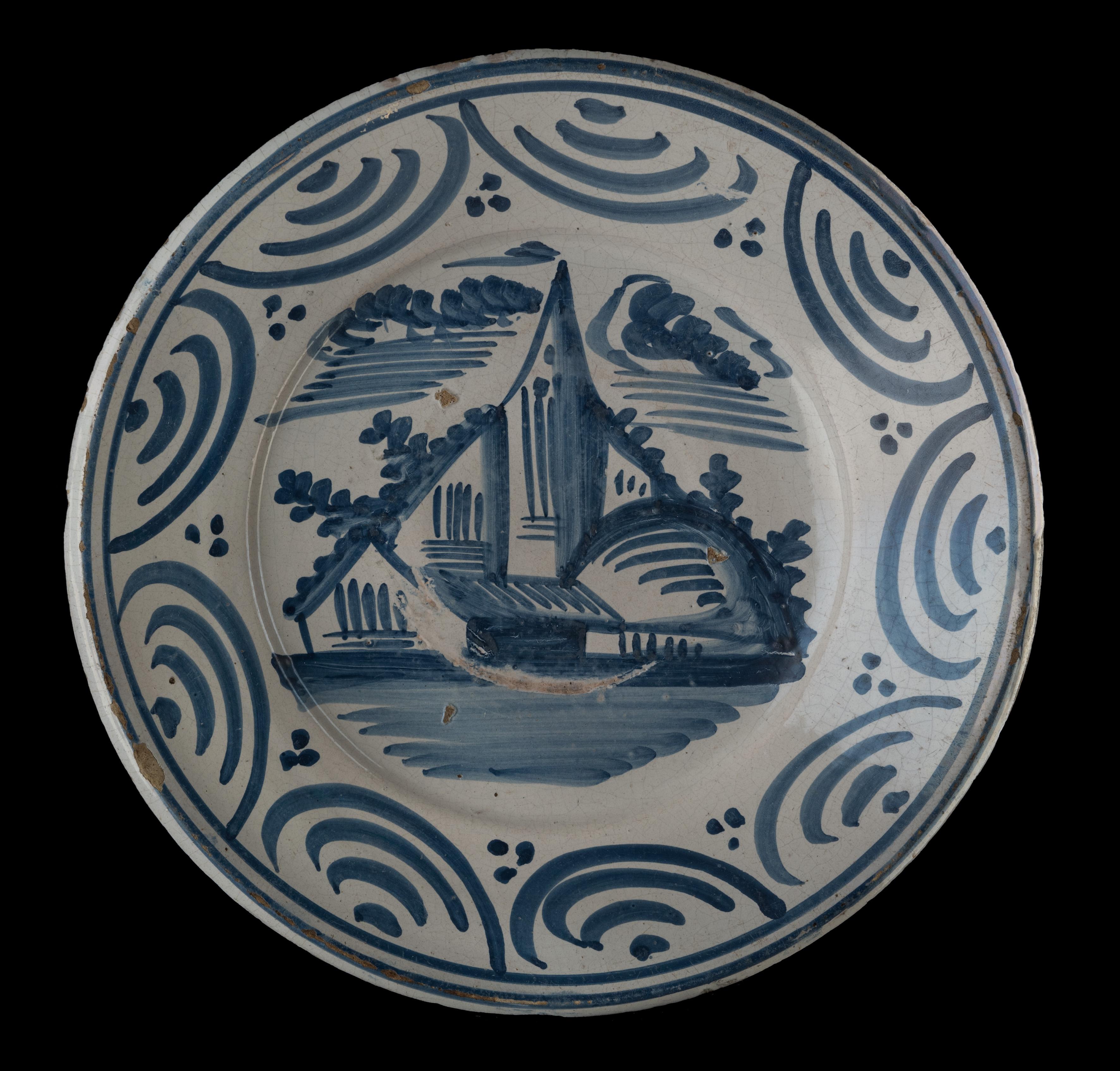 Blue and white landscape dish. Makkum, 1775-1800 
Tichelaar pottery. painter: Douwe Klases Hofstra [attributed to]

The dish has a wide and raised flange and is painted in blue with a simplified village view. The border decor is made up of arched