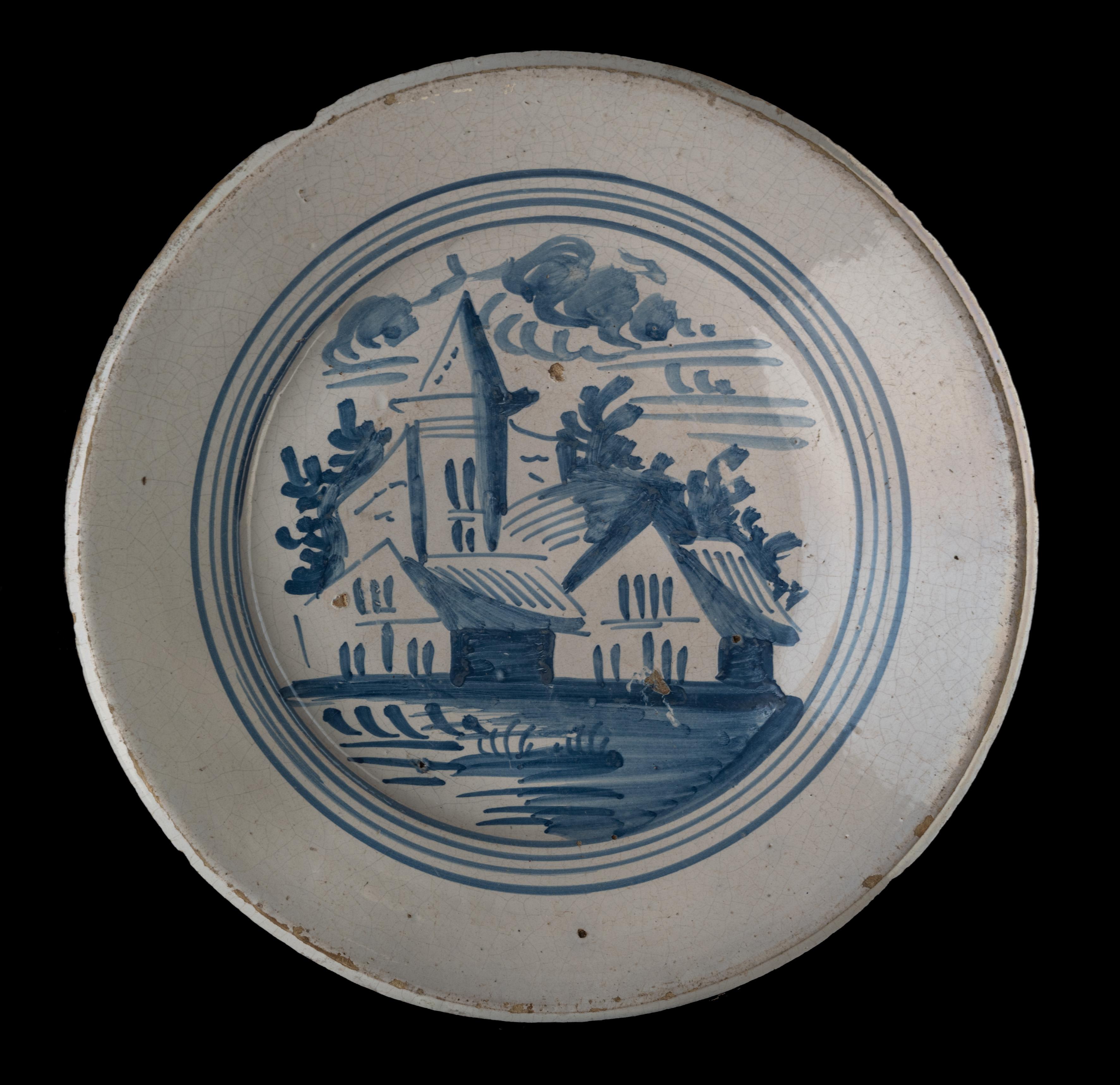 Blue and white landscape dish. Makkum, 1775-1800 
Tichelaar pottery. painter: Douwe Klases Hofstra [attributed to] 

The dish has a wide and raised flange and is painted in blue with a simplified village view, framed within four circles. The