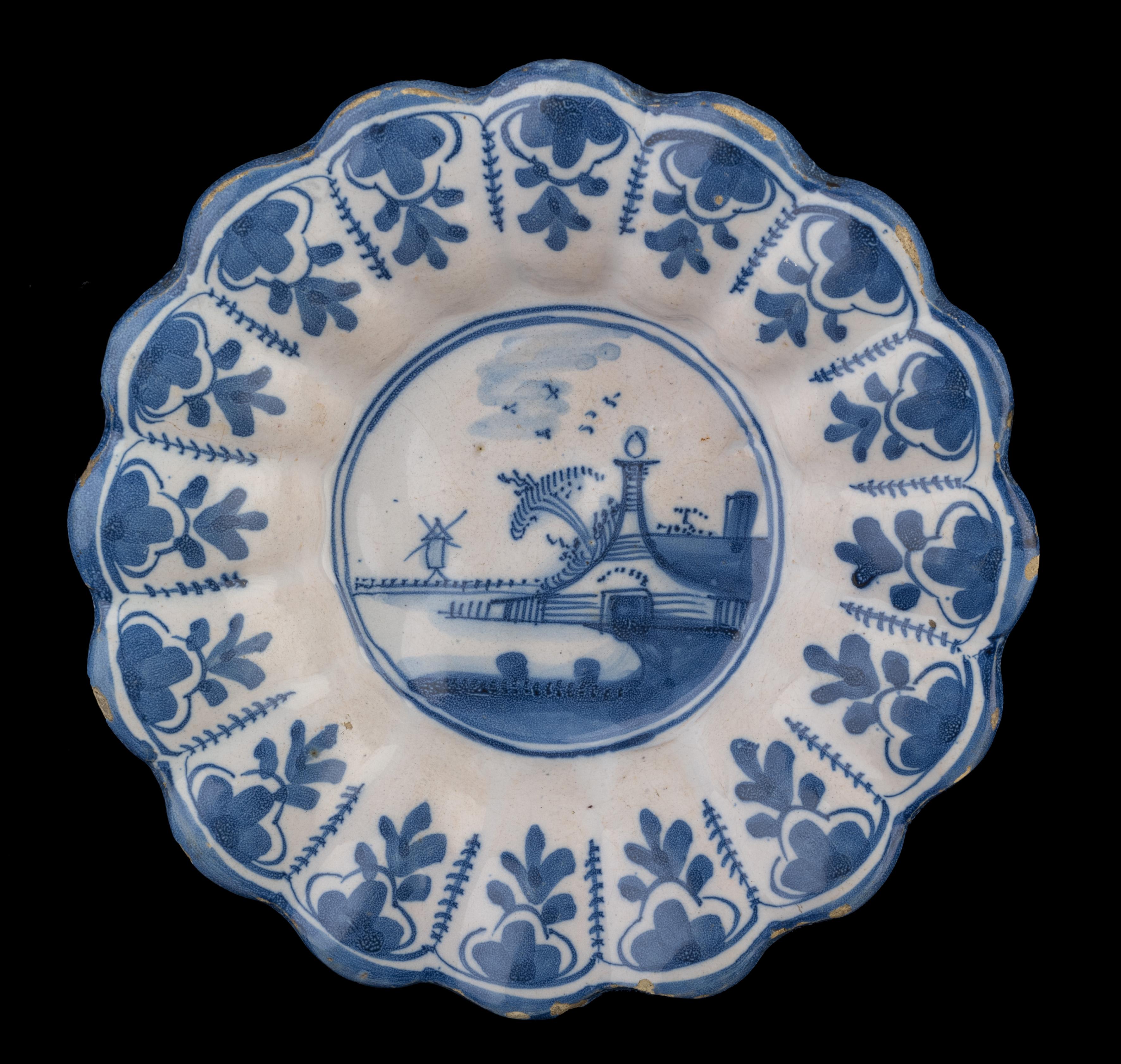 Blue and white lobed dish with landscape. Northern Netherlands, 1650-1680.
Dimensions: diameter 21,5 cm / 8.46 in.

The blue and white lobed dish is composed of sixteen small lobes and is painted in the centre with a landscape. In the background