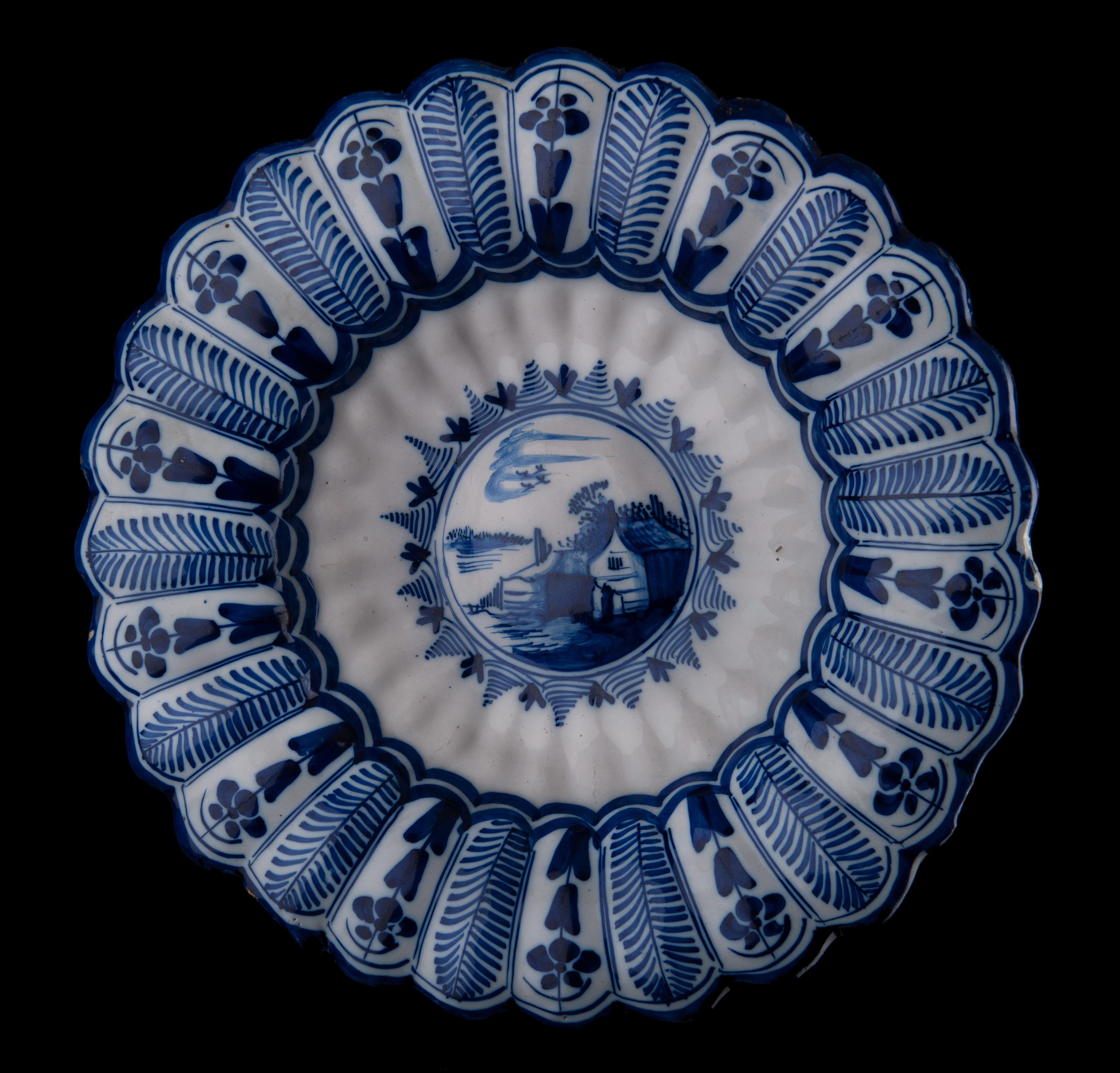 Blue and white lobed dish with landscape. Northern Netherlands, 1650-1680.
Dimensions: diameter 33 cm / 13 in. 

The blue and white dish is composed of twenty-seven double lobes around a curved center. It is painted with a house and barn along