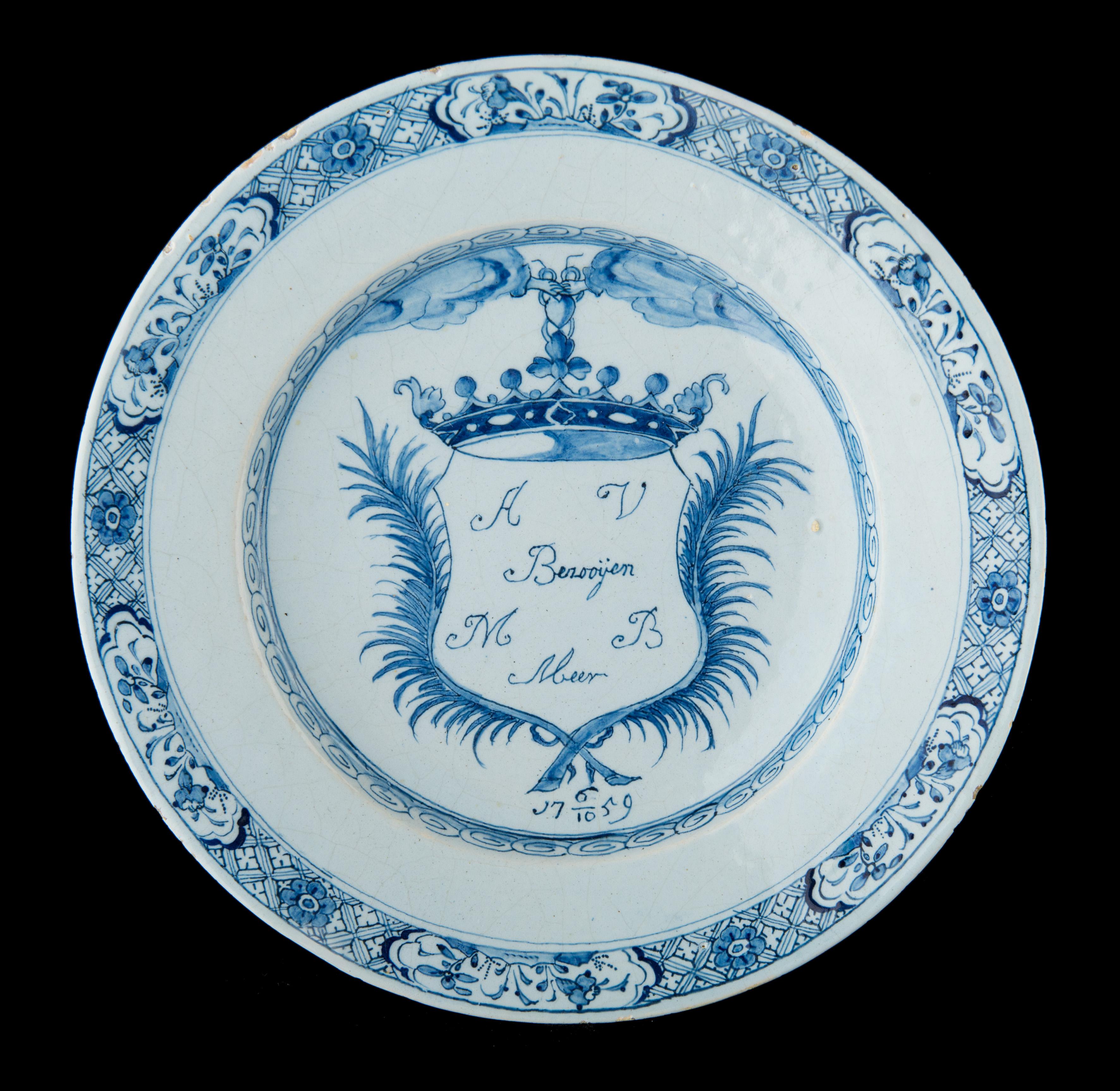 Blue and white marriage plate
Delft, dated 1759

The marriage plate is painted in blue with a crowned shield between two laurel wreaths. The shield is suspended from a heart held by two hands emerging from clouds on either side. The names of the