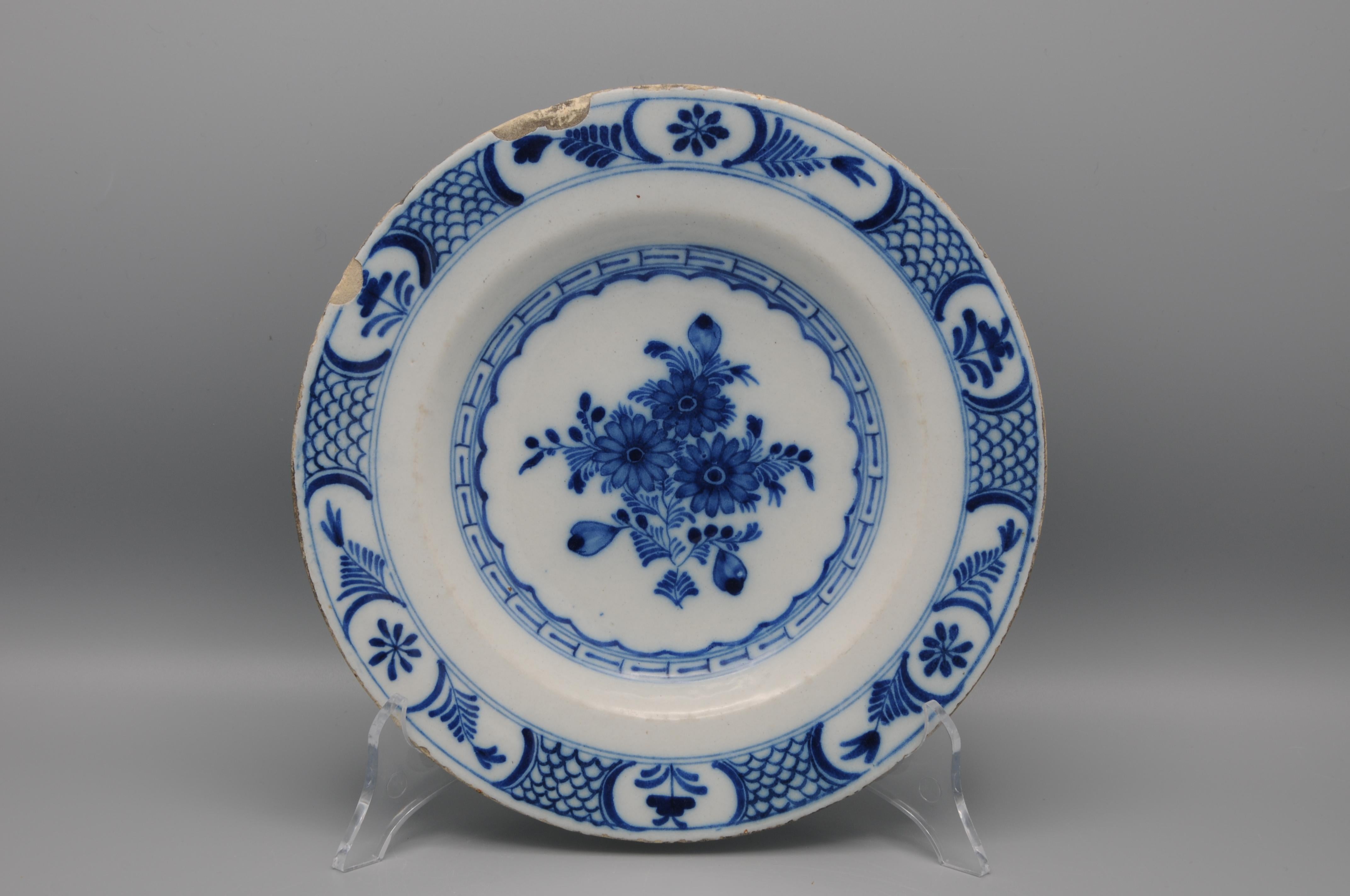 Delft faience plate with blue decoration of a central flower arrangement. The border with stylized flowers in cartouches and a diaperwork. 

Very good condition: usual wear and some larger chipping to the rim
