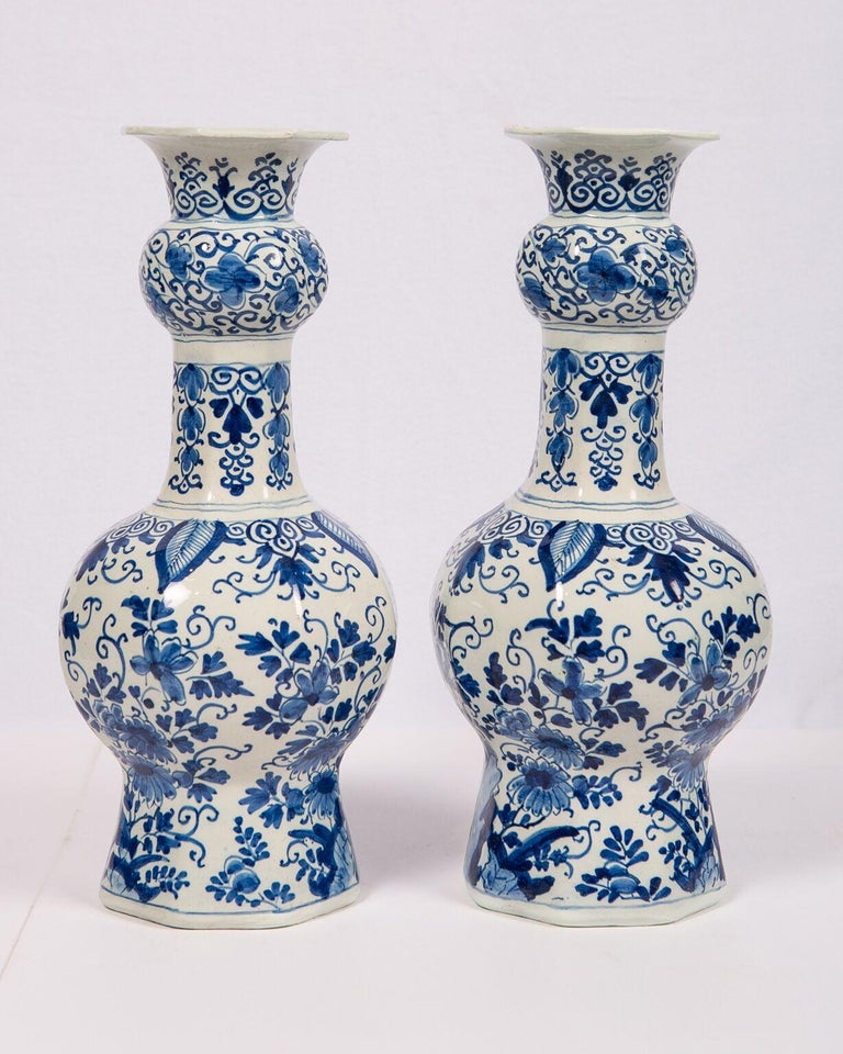 We are pleased to offer this exquisite pair of Dutch delft blue and white vases hand painted in shades of cobalt blue with a continuous scene of songbirds standing on rocky outcroppings surrounded by flowers, leaves, and scrolling vines. The design