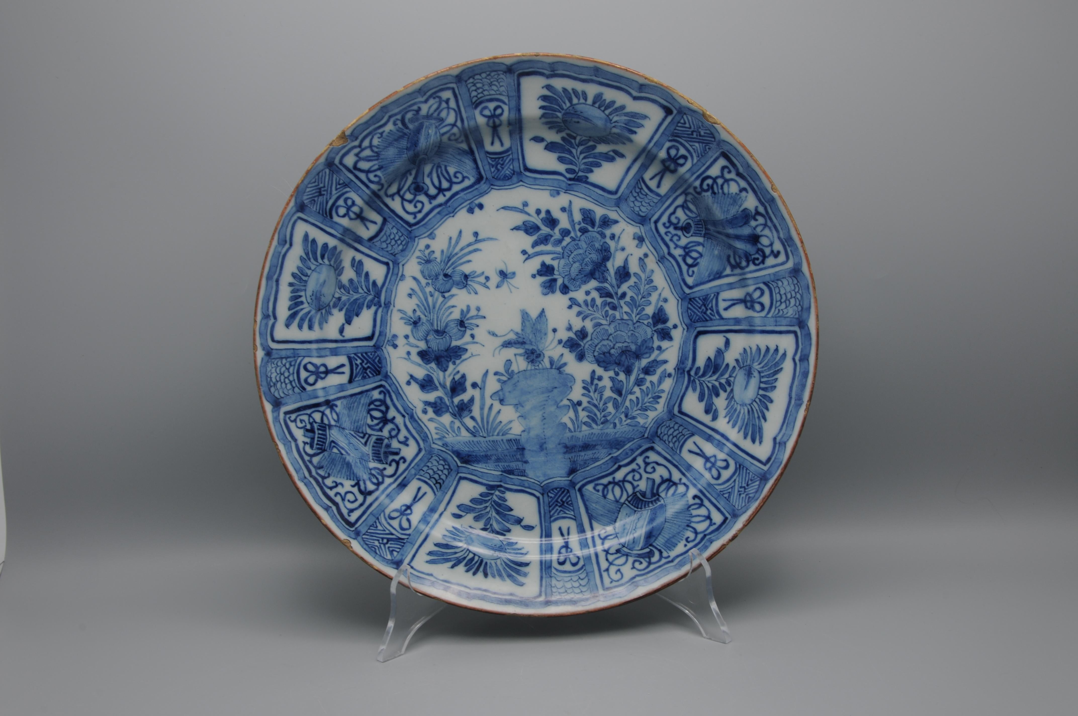 Niederländisches Delft Chinoiserie Ladegerät im Kraak-Stil mit einer großen Libelle, die in einem chinesischen Garten auf einem Felsen sitzt. Alles innerhalb einer achteckigen Umrandung. 
Der Rand ist mit fächerförmigen Feldern versehen, auf denen