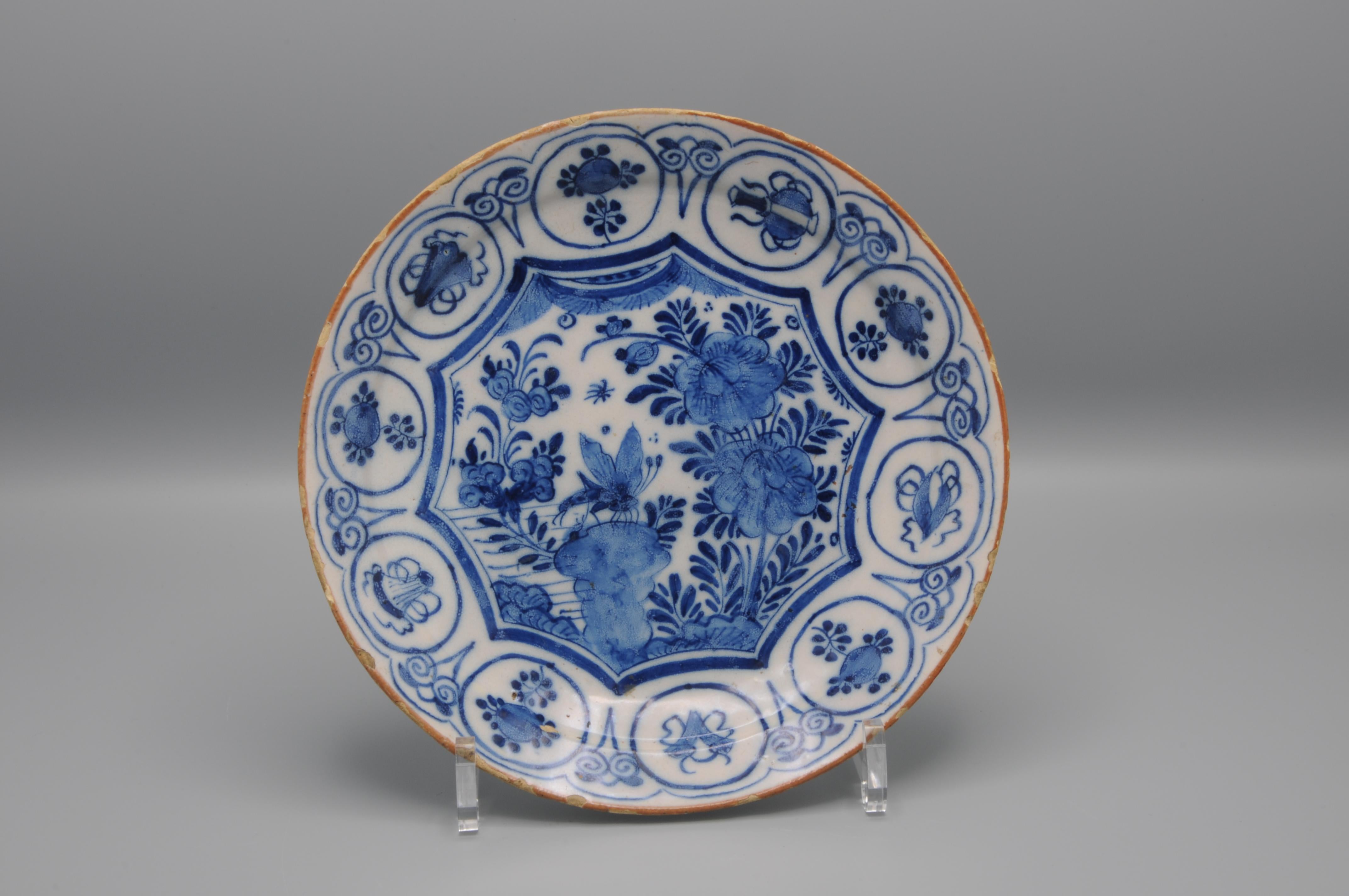 Dutch Delft Chinoiserie plate depicting a large dragonfly, in a Chinese garden, sitting on a rock. All within a shaped octagonal border. The rim in brond and the wide border with a series of roundels depicting stylized flower heads and bugs.
The