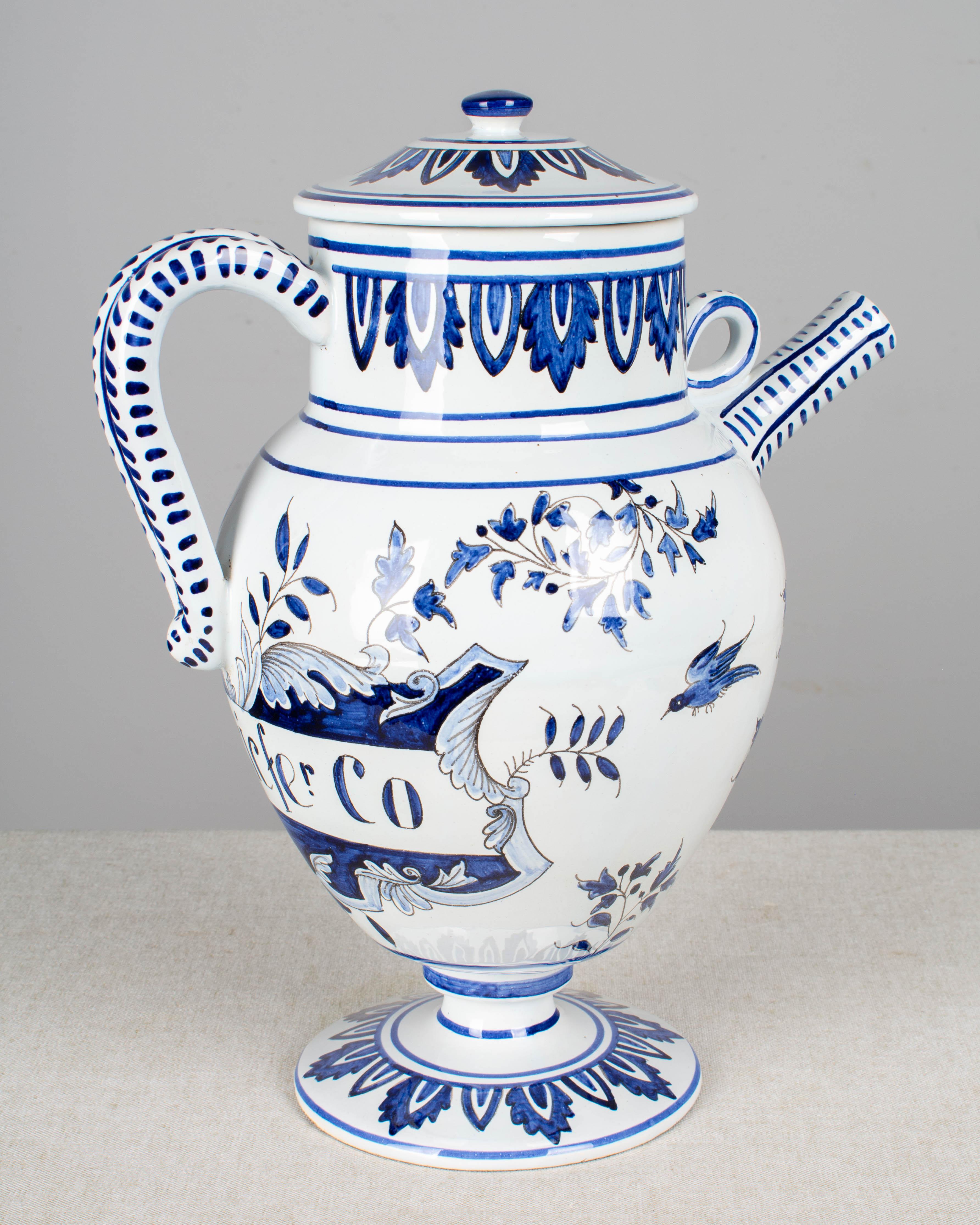 A delft apothecary jug, or pitcher, in the style of the 17th century with striped handle, narrow spout and lid. Hand painted in vivid blue with birds and flowers and decorative label under the handle: S. Decicfer. Co. Mark on bottom: AK.