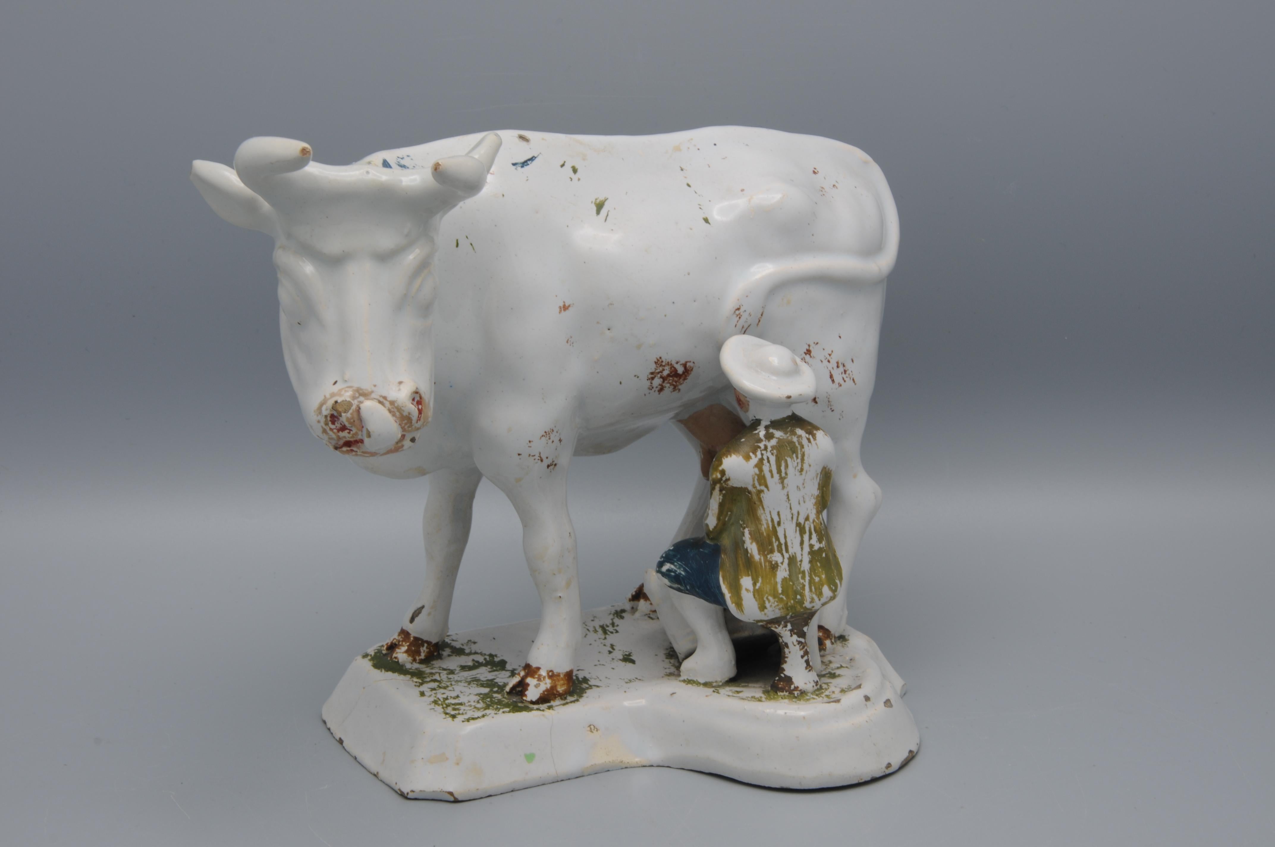 Groupe de traite hollandais en faïence étamée de Delft du XVIIIe siècle, représentant une vache debout et un trayeur assis à ses côtés, décoré de pigments peints à froid appliqués après la cuisson. 

La figure est formée sur une base rectangulaire à