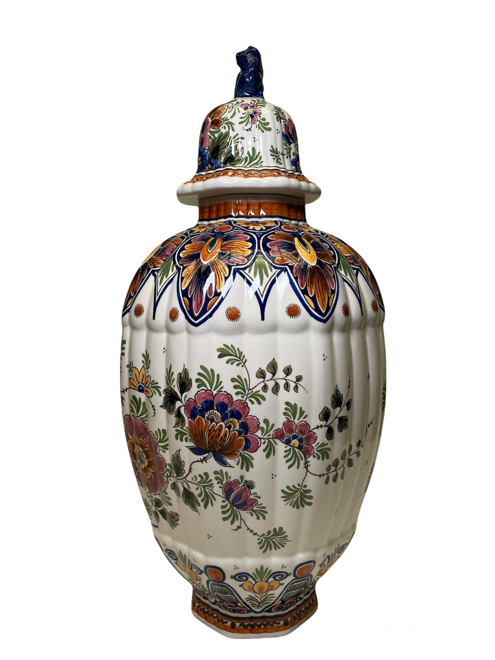 This is a Delft hand painted colorful porcelain lidded ovoid shaped urn vase. It is also reeded with a scalloped border at the upper and bottom area. The vase is adorned with a peacock over a branch of flowers followed by different large and small