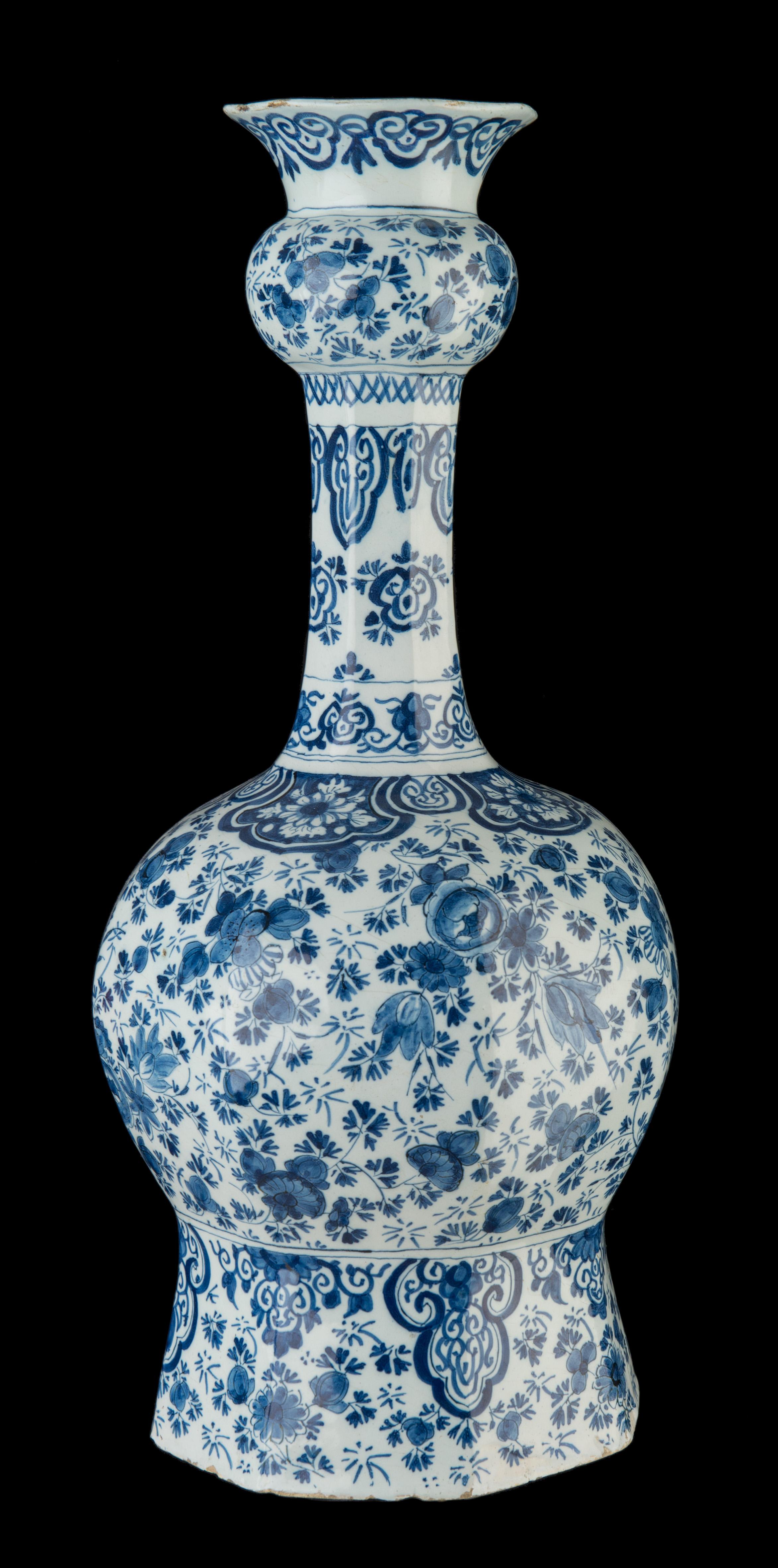 Large blue and white garlic-head bottle vase, delft, 1720-1750.
The octagonal bottle vase stands on a wide, spreading foot with a tall garlic neck over a spherical body ending in a trumpet-shaped mouth. It is painted in blue with floral motifs and