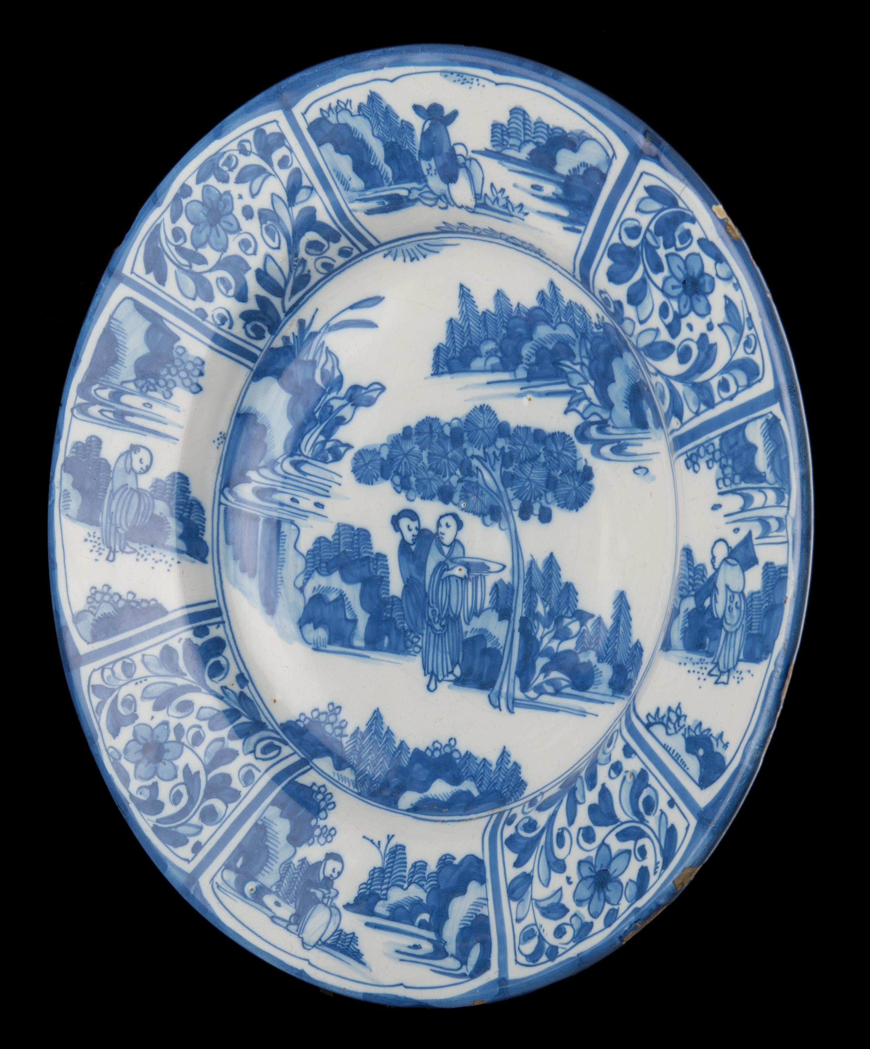 Blaue und weiße Chinoiserie-Schale. Delft, um 1670 

Blau-weiße Schale mit breitem Flansch, in der Mitte zwei sich unterhaltende Chinesen unter einem Baum in einer orientalischen Landschaft. Ein Mann trägt eine Schüssel. Die achtteilige Bordüre ist