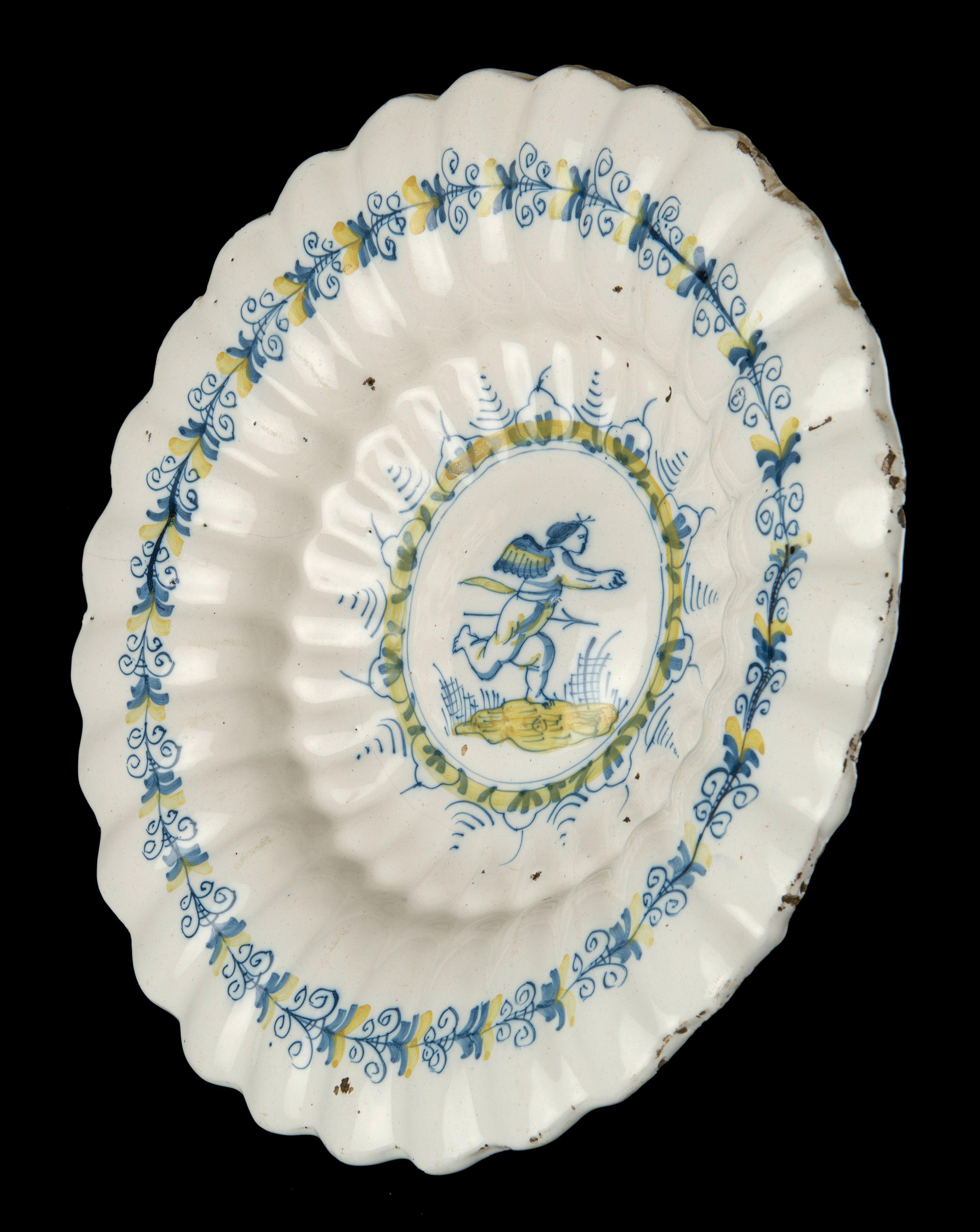 The lobed dish is composed of twenty-seven double lobes and is painted in blue and yellow with a running putto with a spear. The depiction is framed in several circles and a band of stylized floral ornaments. An aigrette motif is applied in the