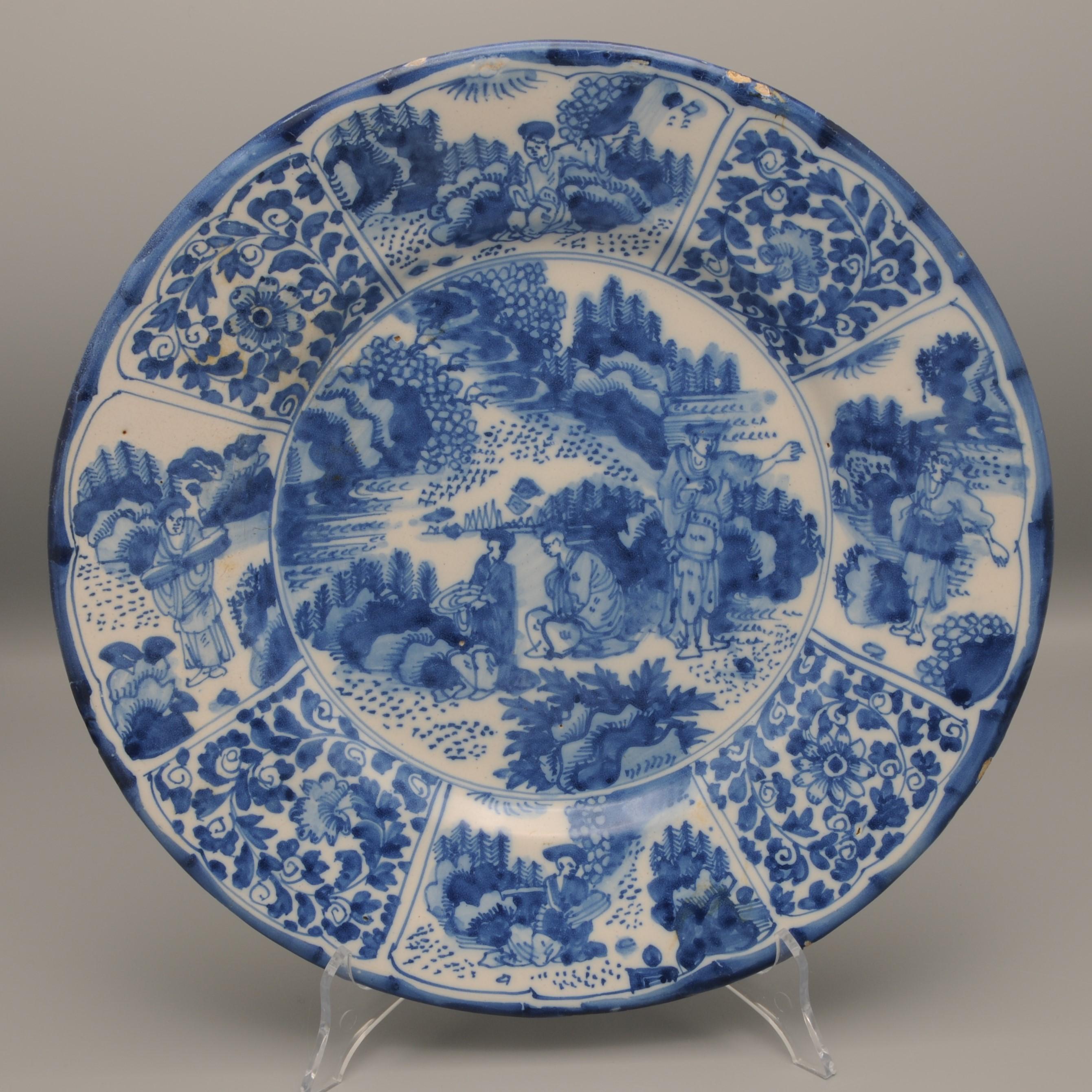 Rare second half 17th century Blue Delftware platter with Chinese kraak style decoration of a garden with 3 Chinese persons. Border decoration in panels. Flower vines in four small panels, seated figures in a landscape in two large panels and two
