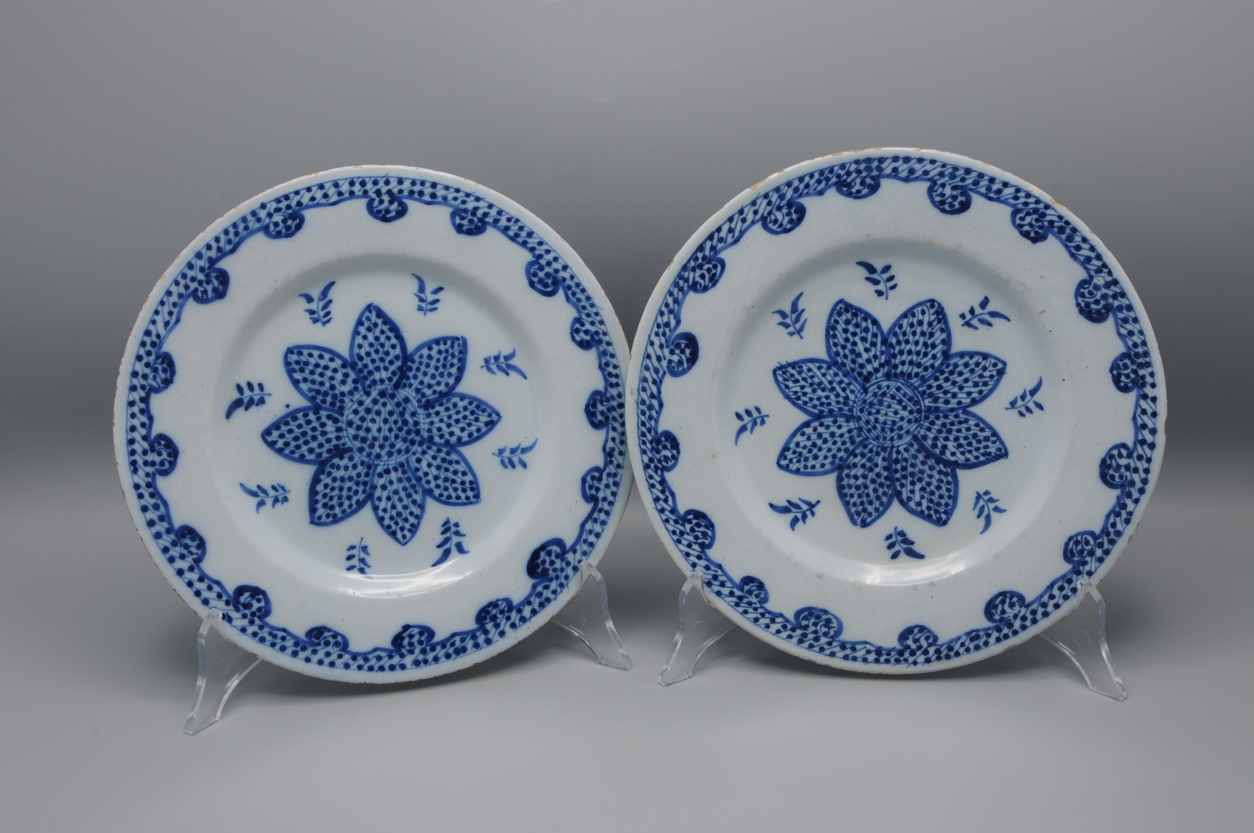 A fine pair of Dutch Delft faience plates, dating to the 18th century, hand-painted in cobalt blue on a tin-glazed white ground. Each plate features a bold central floral rosette with radiating petals filled in a characteristic stippled design,