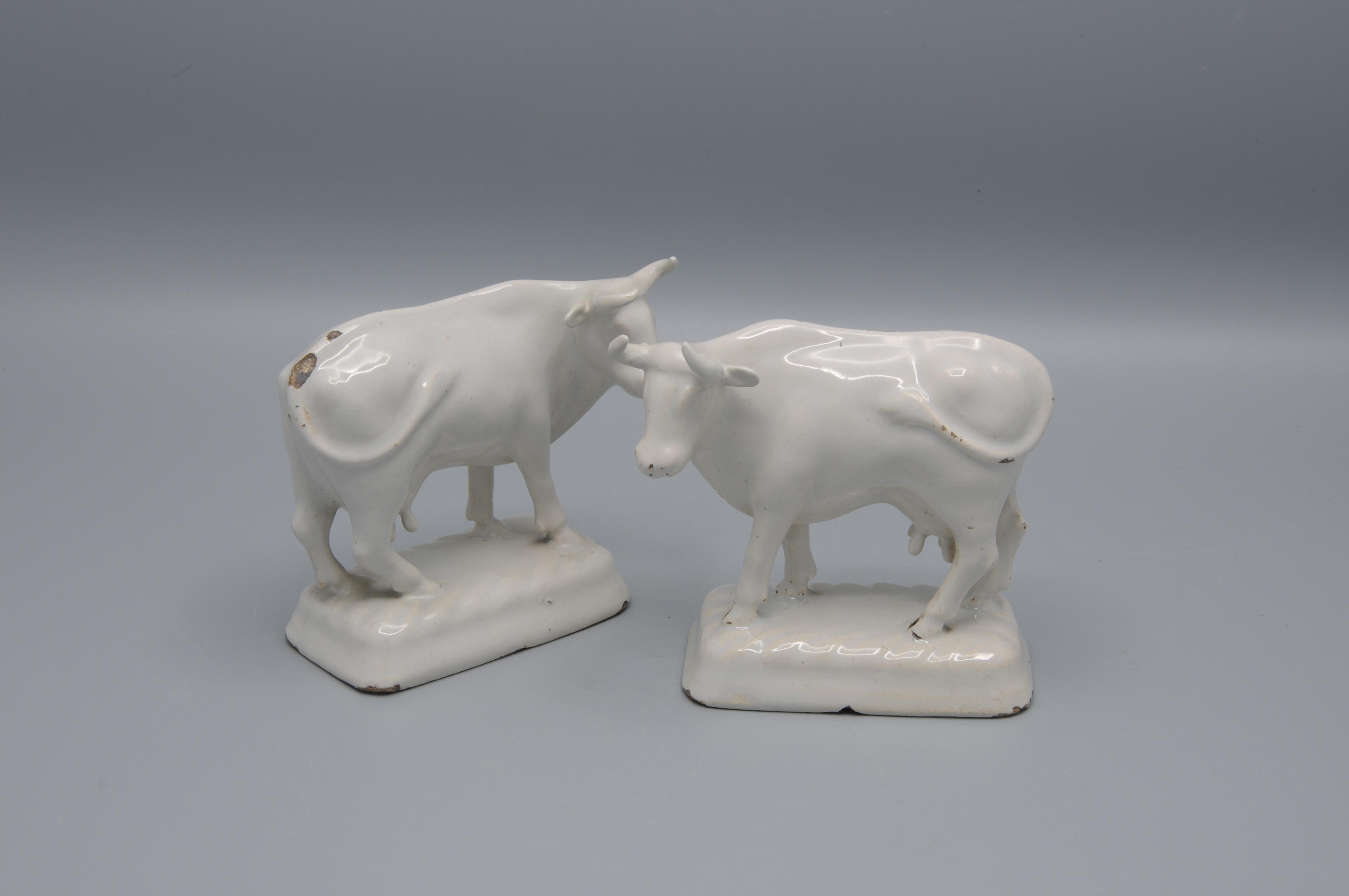 This pair of Delftware cow figurines, dating to the late 18th century, exemplifies the Dutch tradition of molded earthenware crafted in the city of Delft. The figures are finished with a tin-glazed white surface, characteristic of Delftware, and are