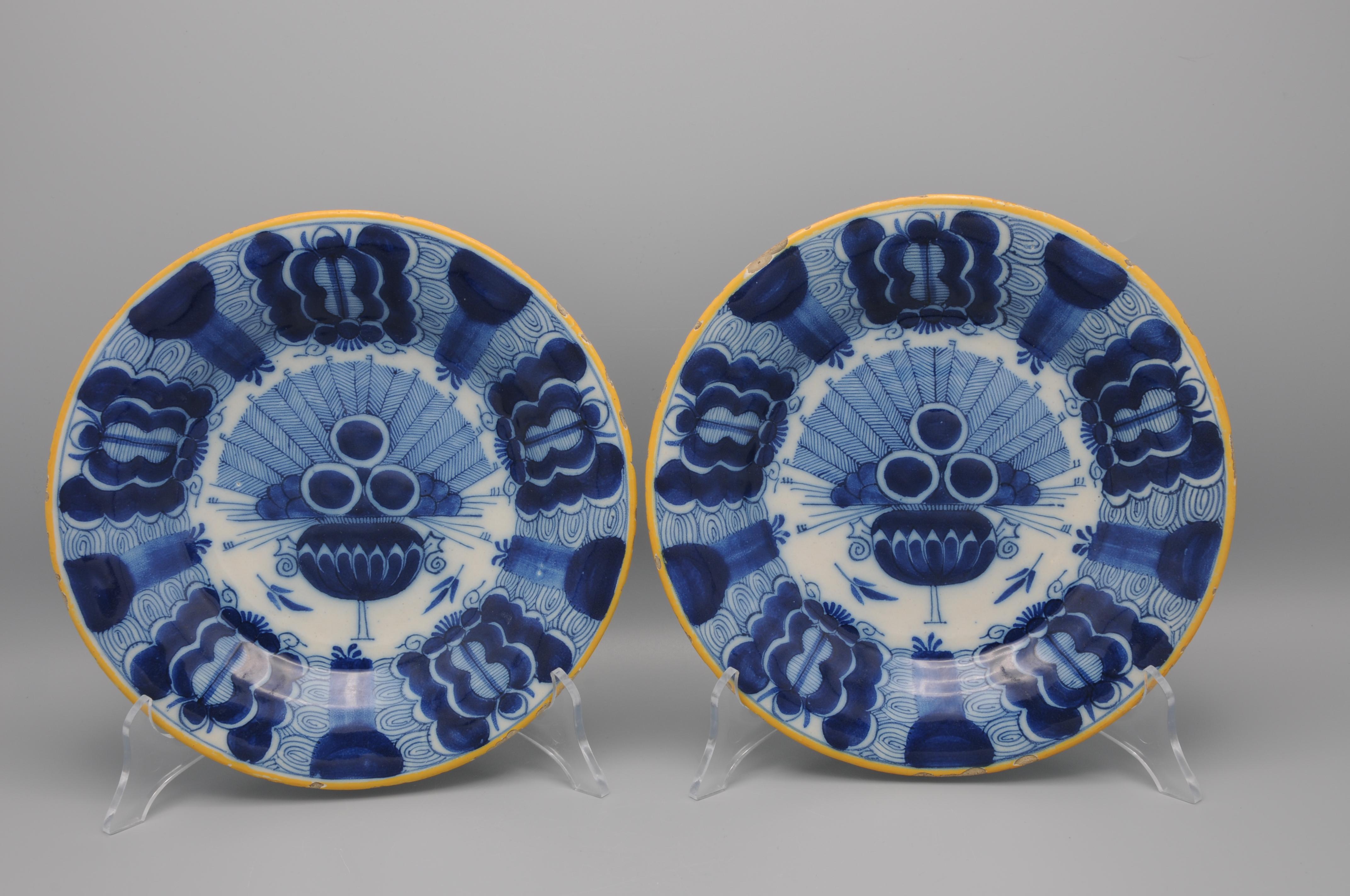 Pair of two Dutch Delft blue and white 'Peacock' plate, 18th century, with ochre rim, the centre decorated in cobalt with an vase containing an arrangement of peacock feathers and flowers. The rim decorated with stylized flower heads against a