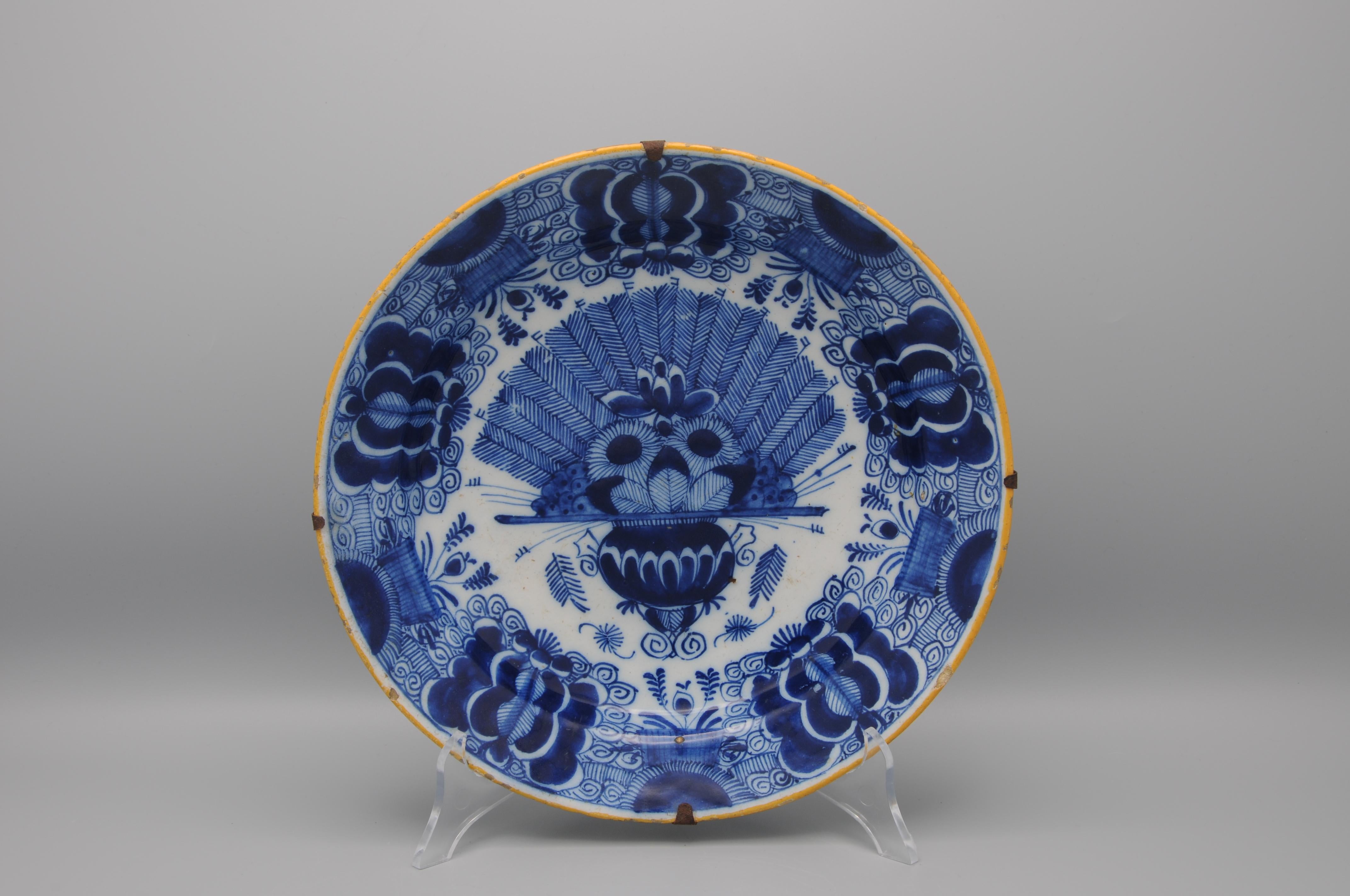 Dutch Delft blue and white 'Peacock' plate, 18th century, with ochre rim, the center decorated in cobalt with an vase containing an arrangement of peacock feathers and flowers. The rim decorated with stylized flower heads against a scrolling ground.
