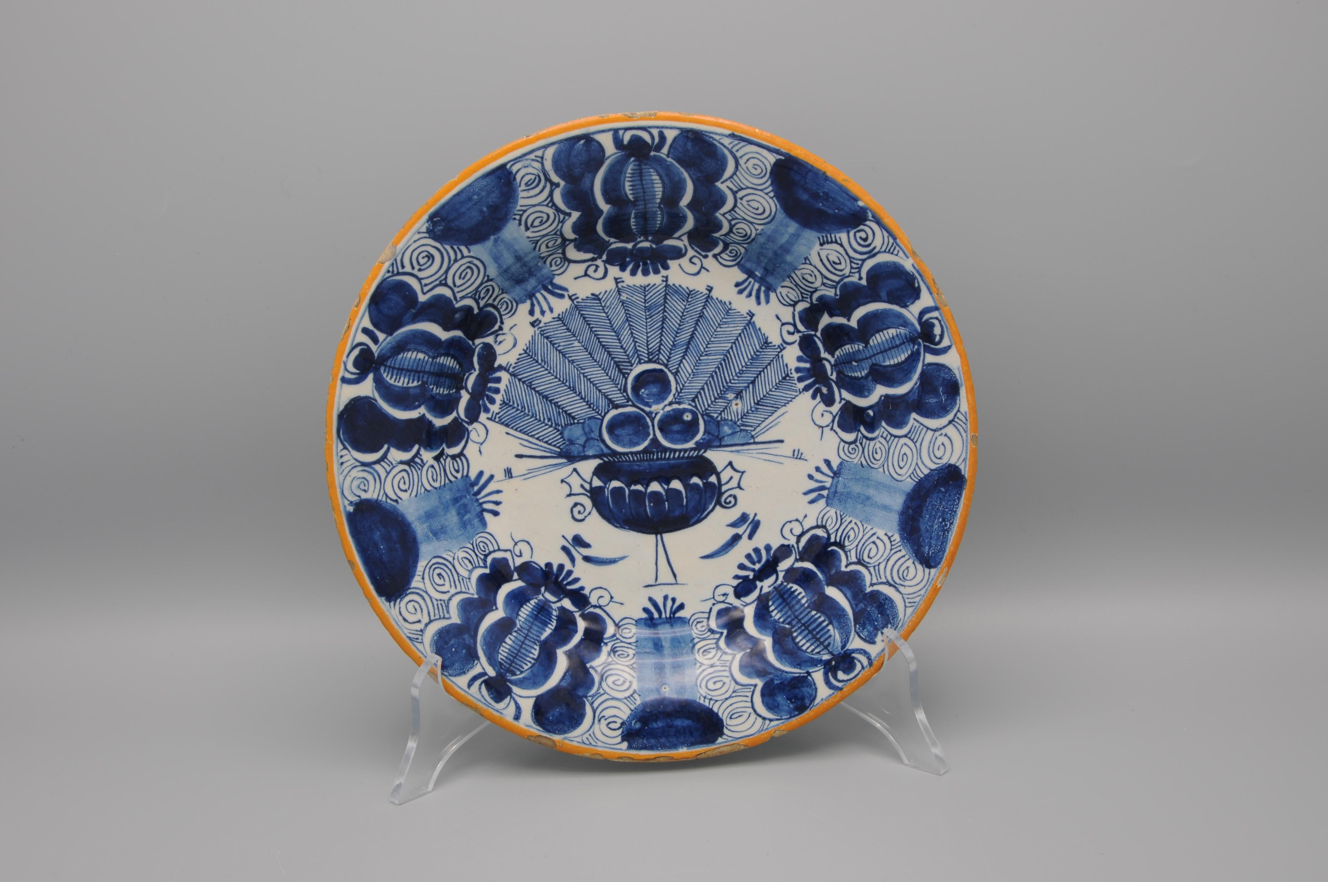 Dutch Delft blue and white 'Peacock' plate, 18th century, with ochre rim, the center decorated in cobalt with an vase containing an arrangement of peacock feathers and flowers. The rim decorated with stylized flower heads against a scrolling ground.