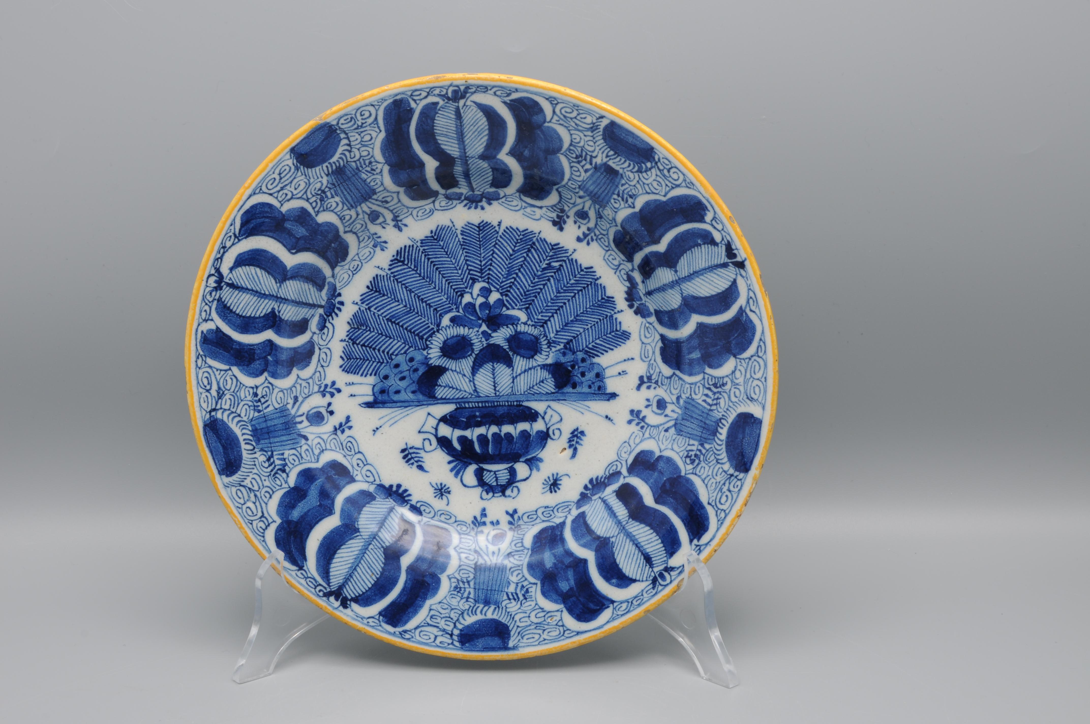 Dutch Delft blue and white 'Peacock' plate, 18th century, with ochre rim, the center decorated in cobalt with an vase containing an arrangement of peacock feathers and flowers. The rim decorated with stylized flower heads against a scrolling ground.