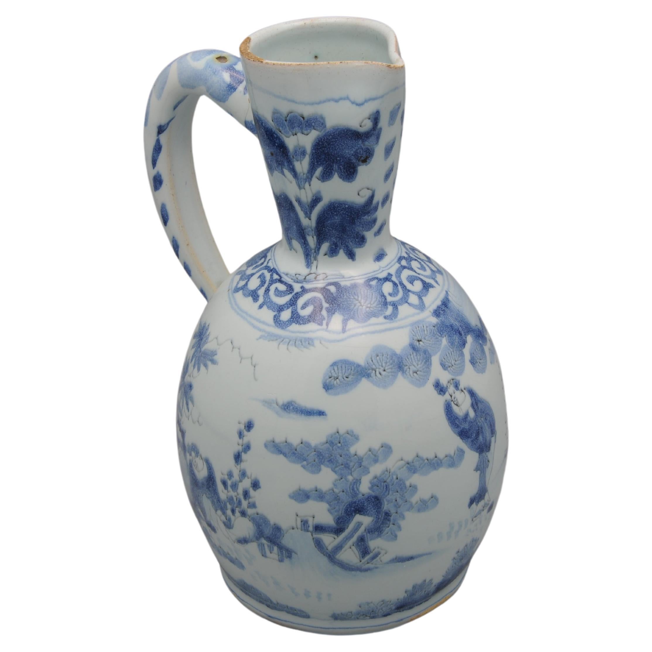 Dutch Delftware pouring jug with soft blue decoration of a chinoiserie landscape with persons. The neck with two stylised flowers above a lambrequin border at the neck, the handle with a scrollwork pattern. Wanli style decoration
