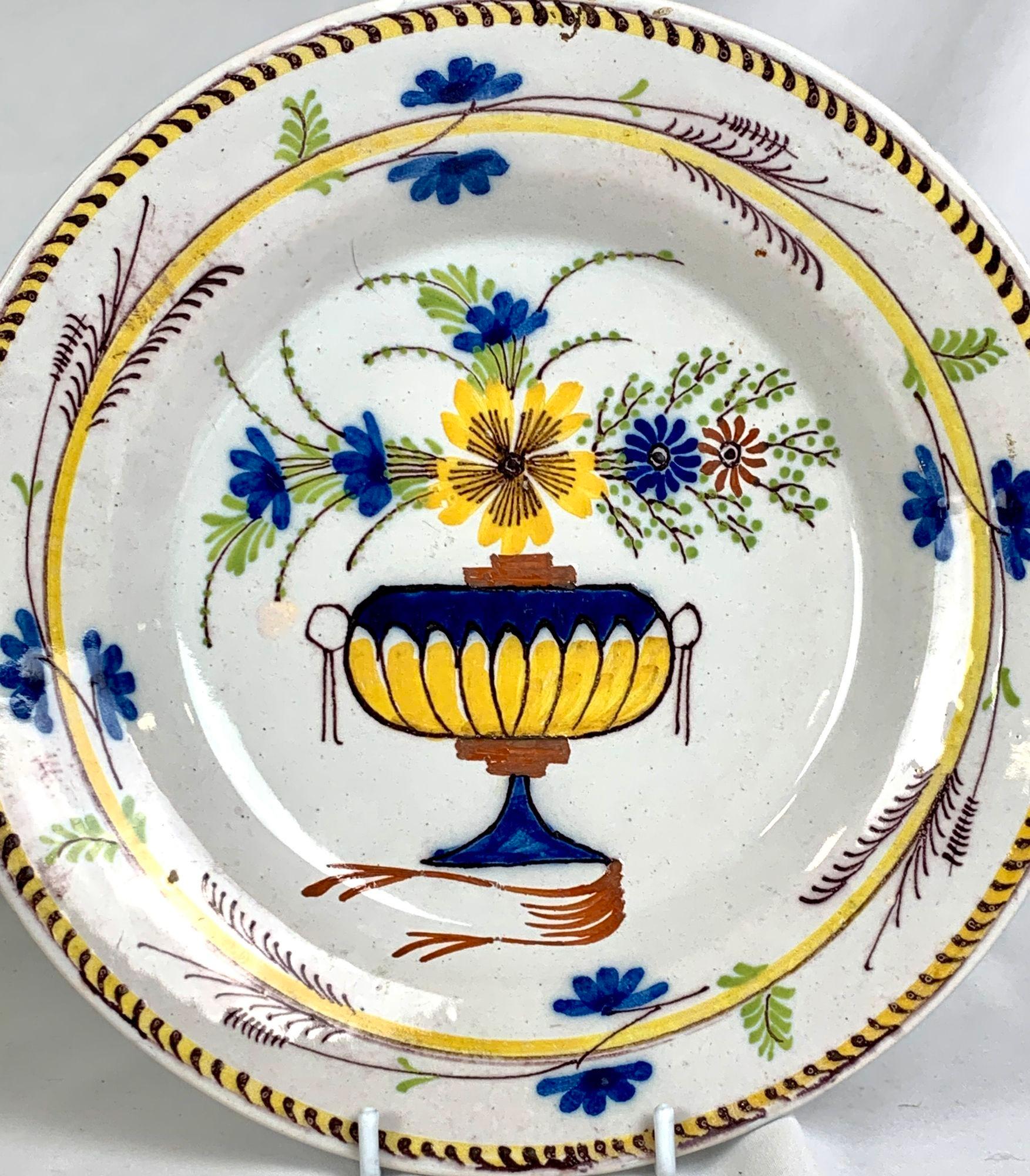 Dieser handbemalte Teller aus dem niederländischen Delft zeigt eine hübsche, mit Blumen gefüllte Vase, die mit leuchtenden Farben in Zitronengelb, Blau, Eisenrot und Violett bemalt ist.
Die leuchtend gelbe Blüte zieht die Aufmerksamkeit auf