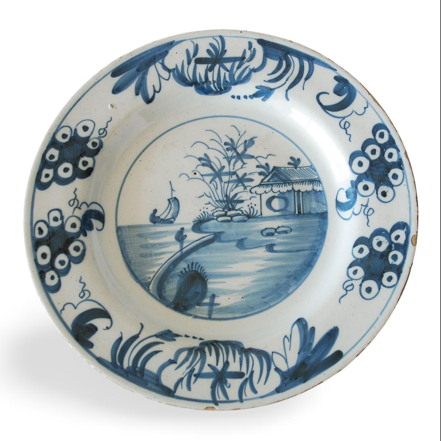A dinner-plate, painted in the delft style, with a ship coming to land; bunches of grapes around the edge.

See Michael Archer, Delftwarem m233 no B258 for a similar example, which he places at Delftfield (Glasgow) on the basis of wasters