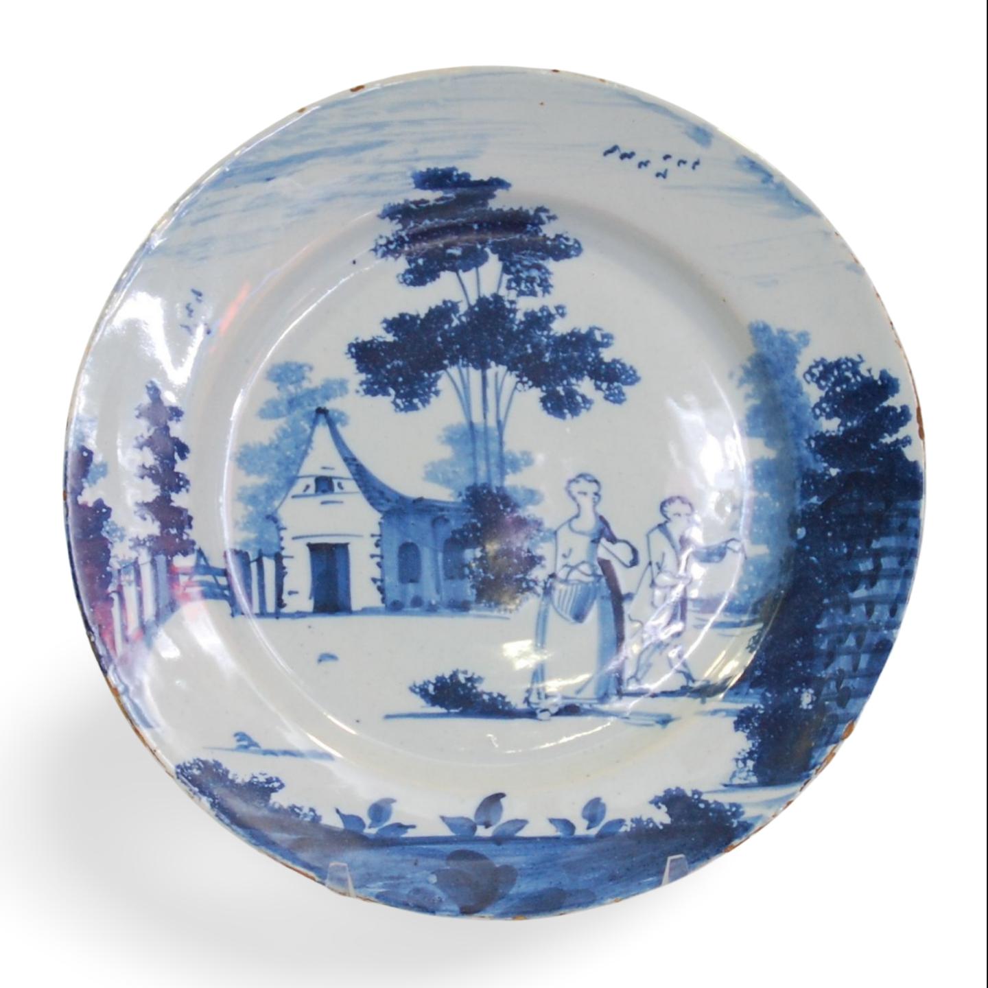 A dinner-plate, painted in the delft style with a couple leacing a church, or perhaps a house. Wincanton pottery, or perhaps London.

English Delftware is considered to be one of the most important forms of English ceramic production of the period,