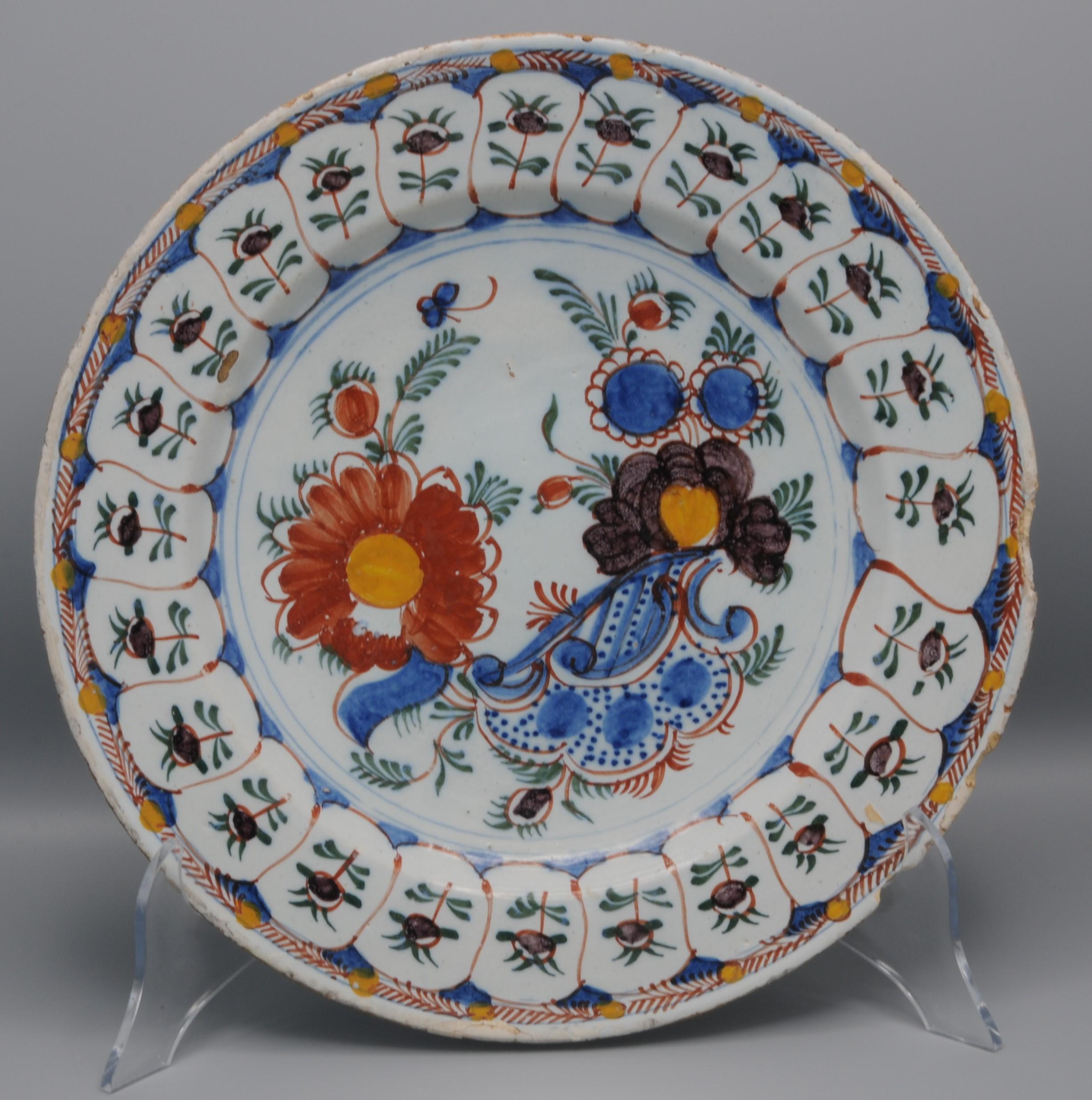 Polychrome (multicolor) Delftware platter with rococo decoration of blossoming flowers and insects above a rocaille ornament. 
Rim decorated with panels depicting flowers 
Unmarked

Fair condition; chipping, some retouched and usual wear to the rim.