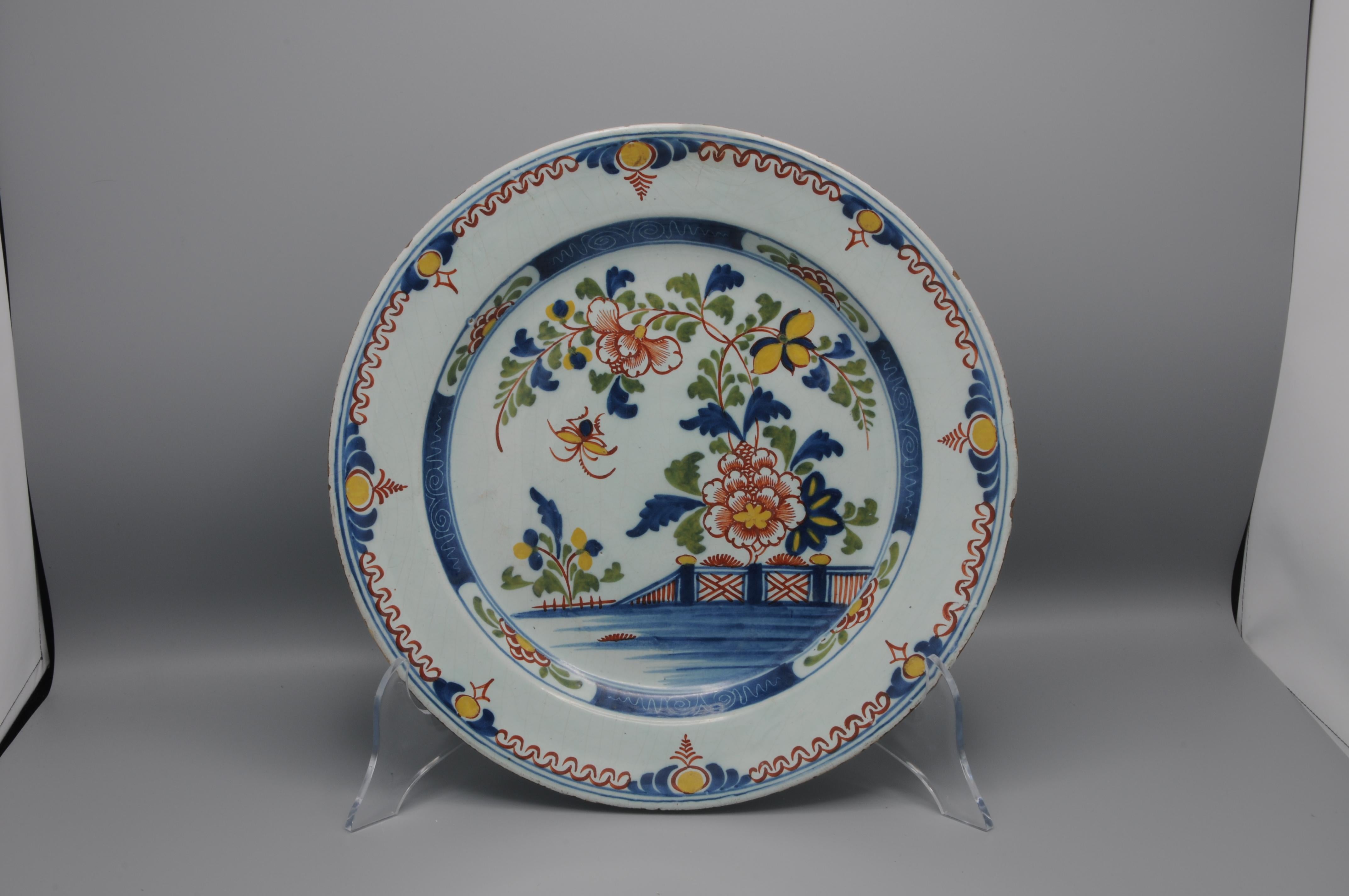 Delft Polychrome Delftware platter with fine chinoiserie decoration of a central depiction of a blossoming peony against a fence.

Unmarked
Fair condition; some chipping professionally restored (see pictures) and slight wear to the rim.