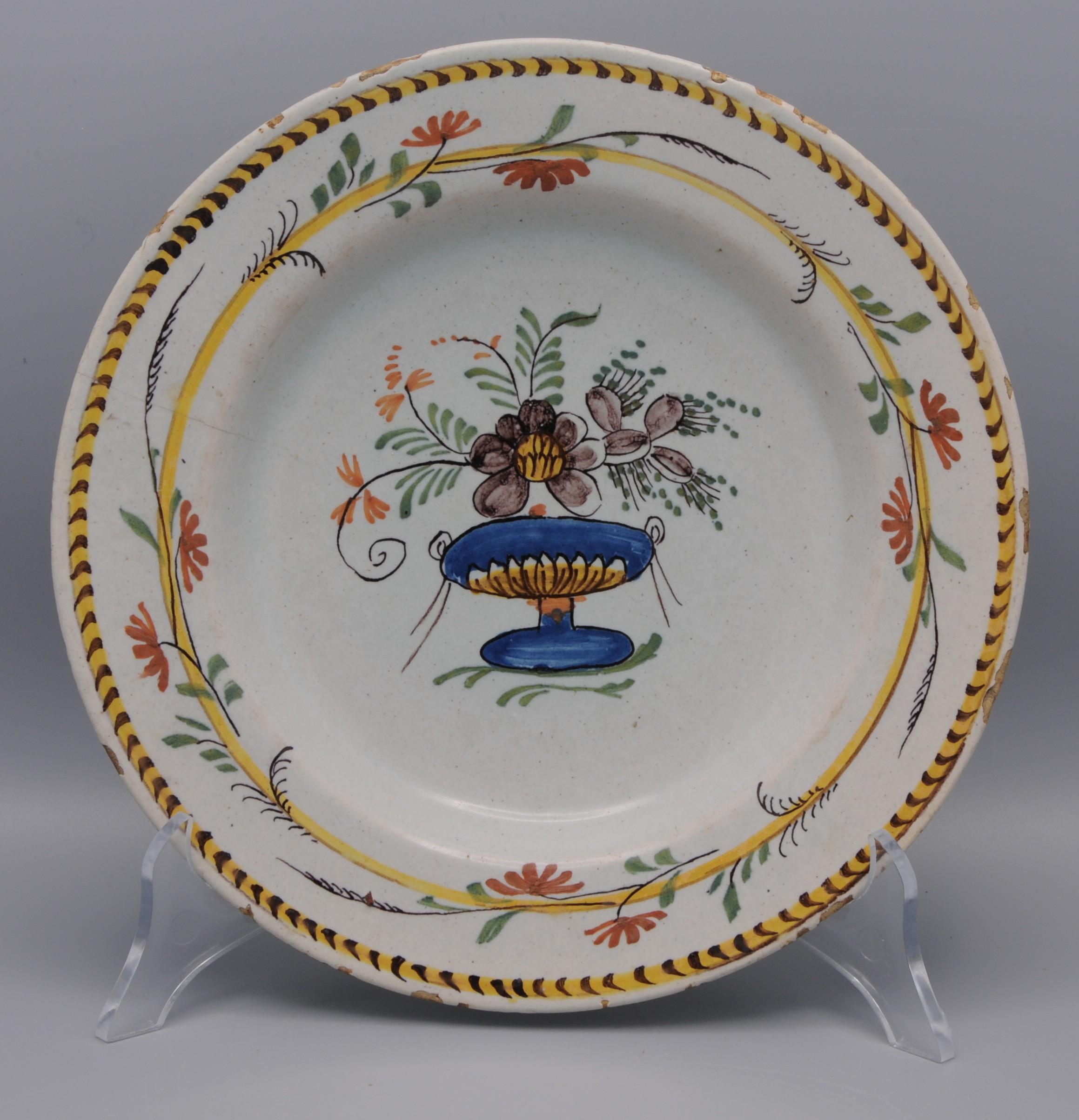 Plato de Delft de finales del siglo XVIII con decoración neoclásica de un jarrón central con manganeso y flores rojas y ramas floridas. El borde está decorado con flores rojas entrelazadas.  

Manganeso y hierro - decoración de bordes rojos. 
Sin