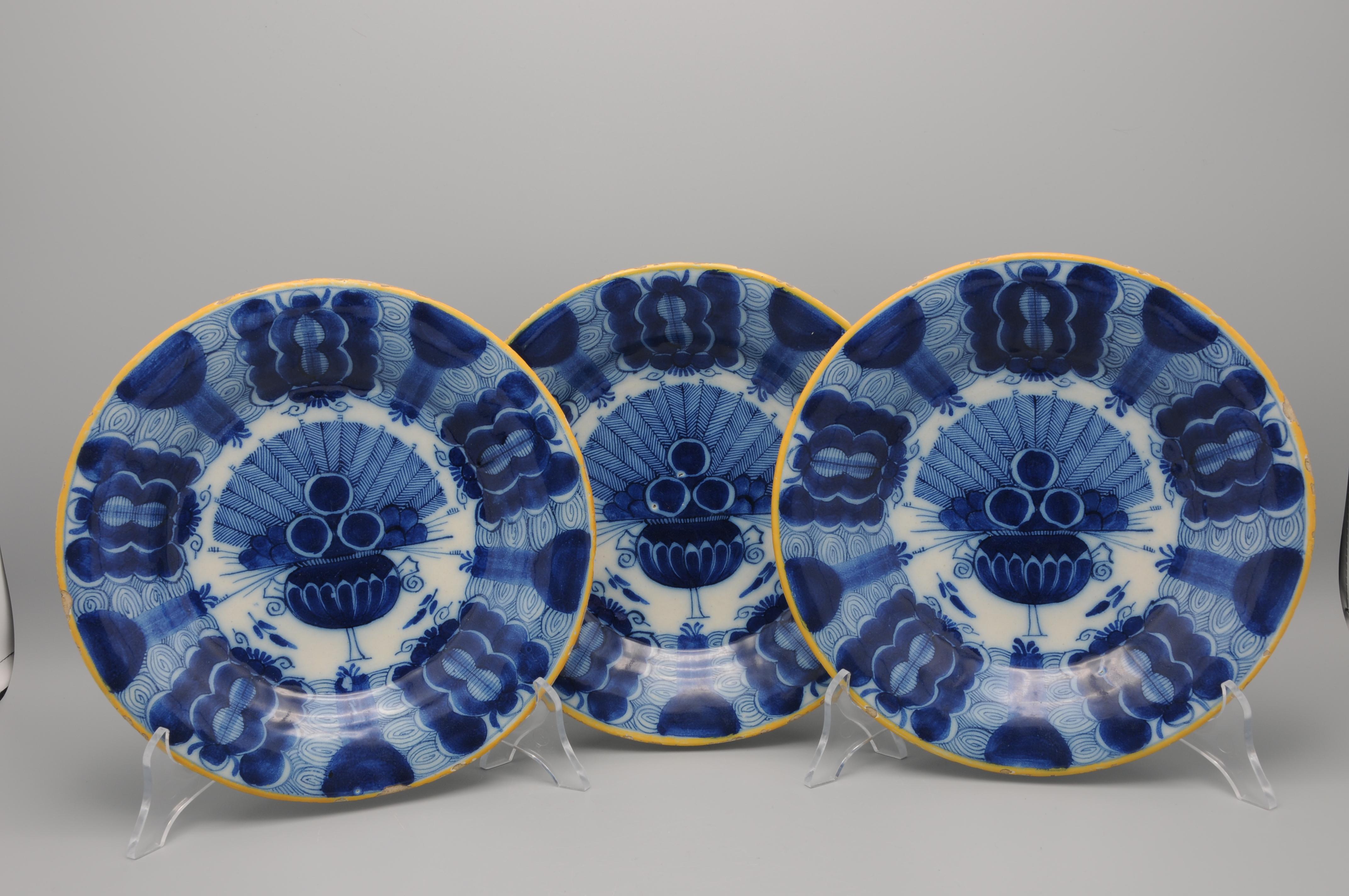 Set of 3 Dutch Delft blue and white 'Peacock' plate, 18th century, with ochre rim, the centre decorated in cobalt with an vase containing an arrangement of peacock feathers and flowers. The rim decorated with stylised flower heads against a