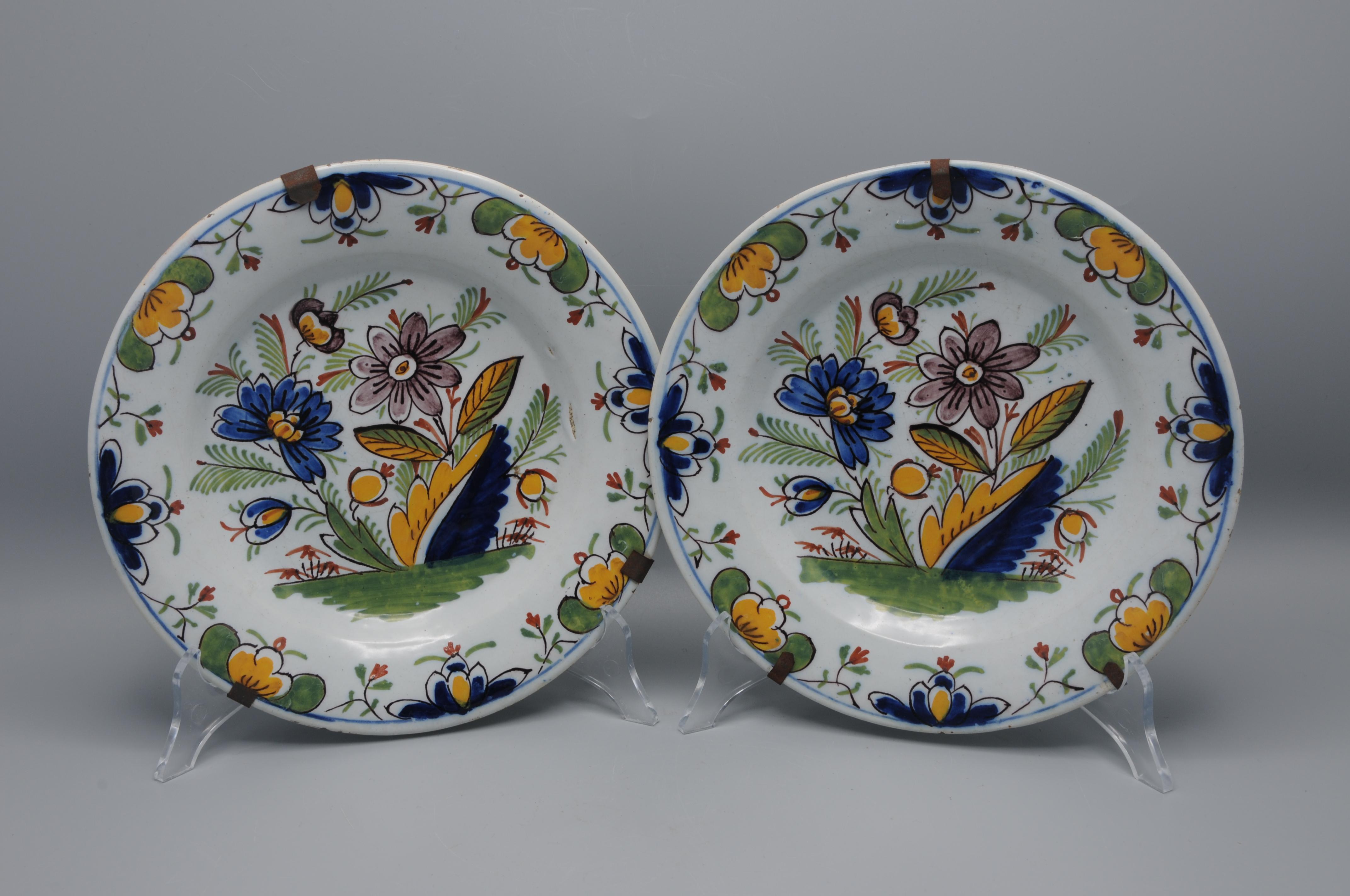 Pair of early 19th-century Dutch polychrome plates, tin-glazed earthenware with polychrome hand-painted decoration. The central motif shows a stylized floral spray with symmetrical leaves and blossoms, surrounded by scrolling foliate elements and
