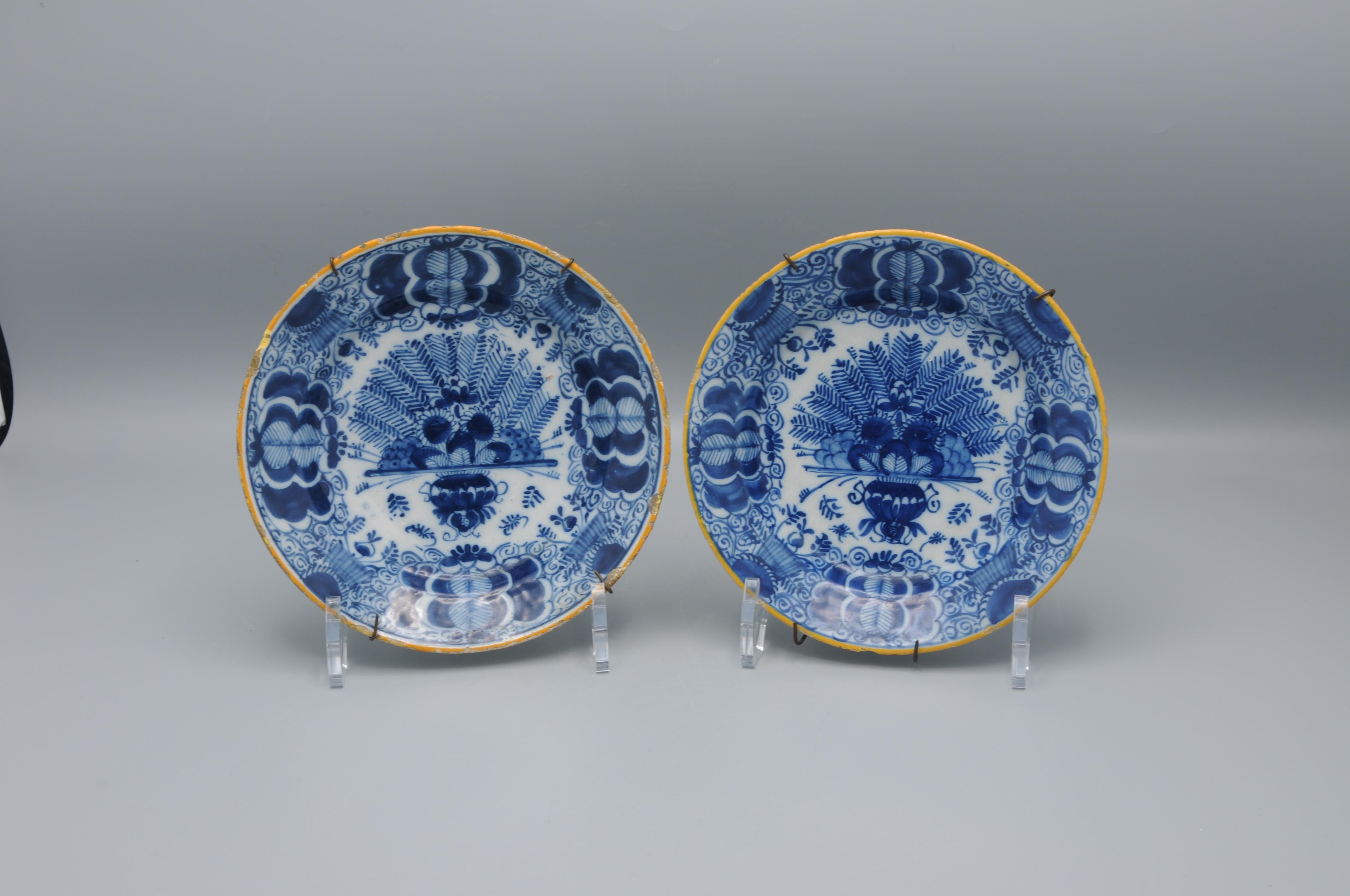 Set of two Dutch Delft blue and white 'Peacock' plates, 18th century, with ochre rim, the centre decorated in cobalt with an vase containing an arrangement of peacock feathers and flowers. The rim decorated with stylized flower heads against a