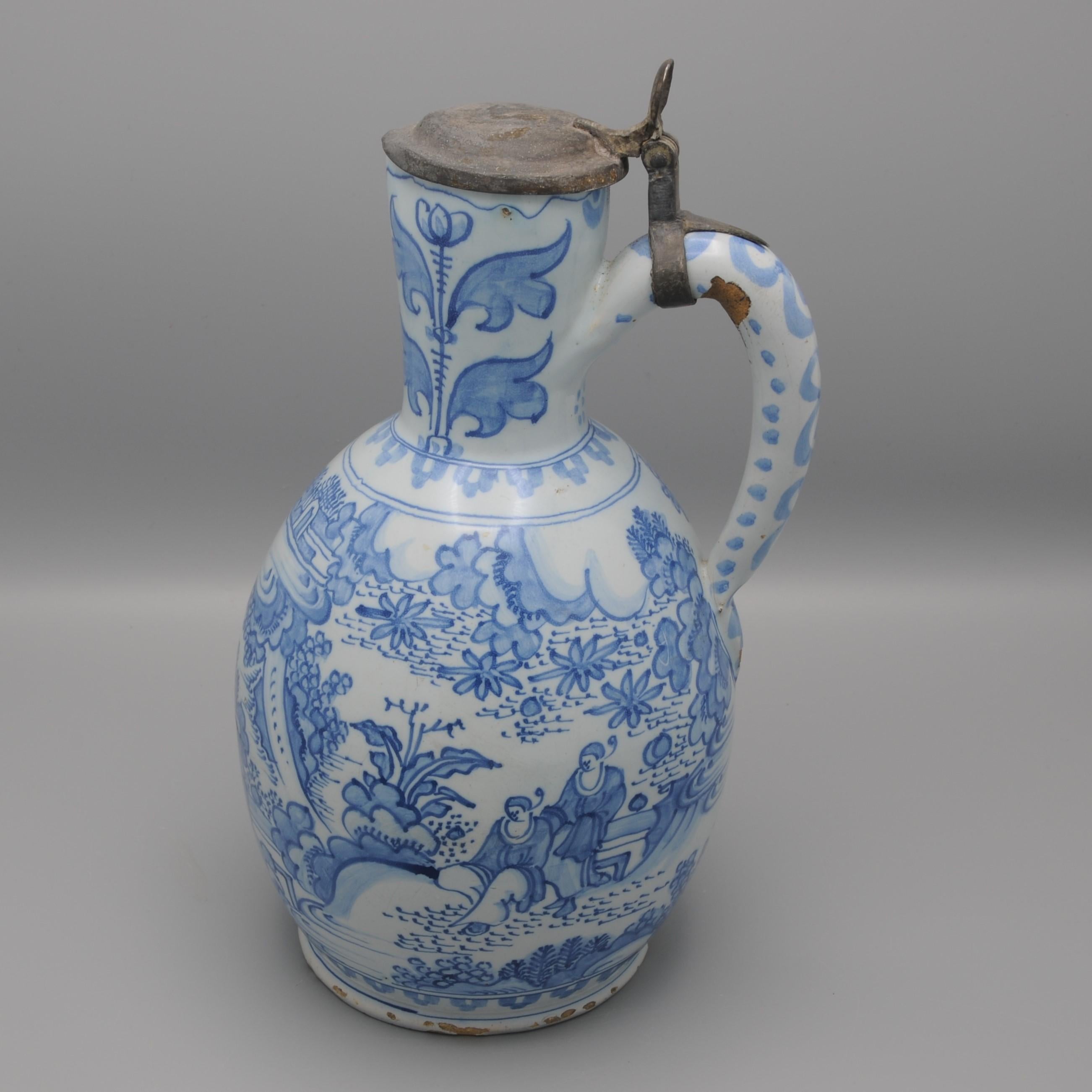 Verseuse en faïence hollandaise, de très grande taille. Décorée en bleu tendre d'un paysage chinois élaboré avec des personnes d'après des motifs de porcelaine wan-li. Le col est orné de deux fleurs stylisées au-dessus d'une bordure de feuilles,