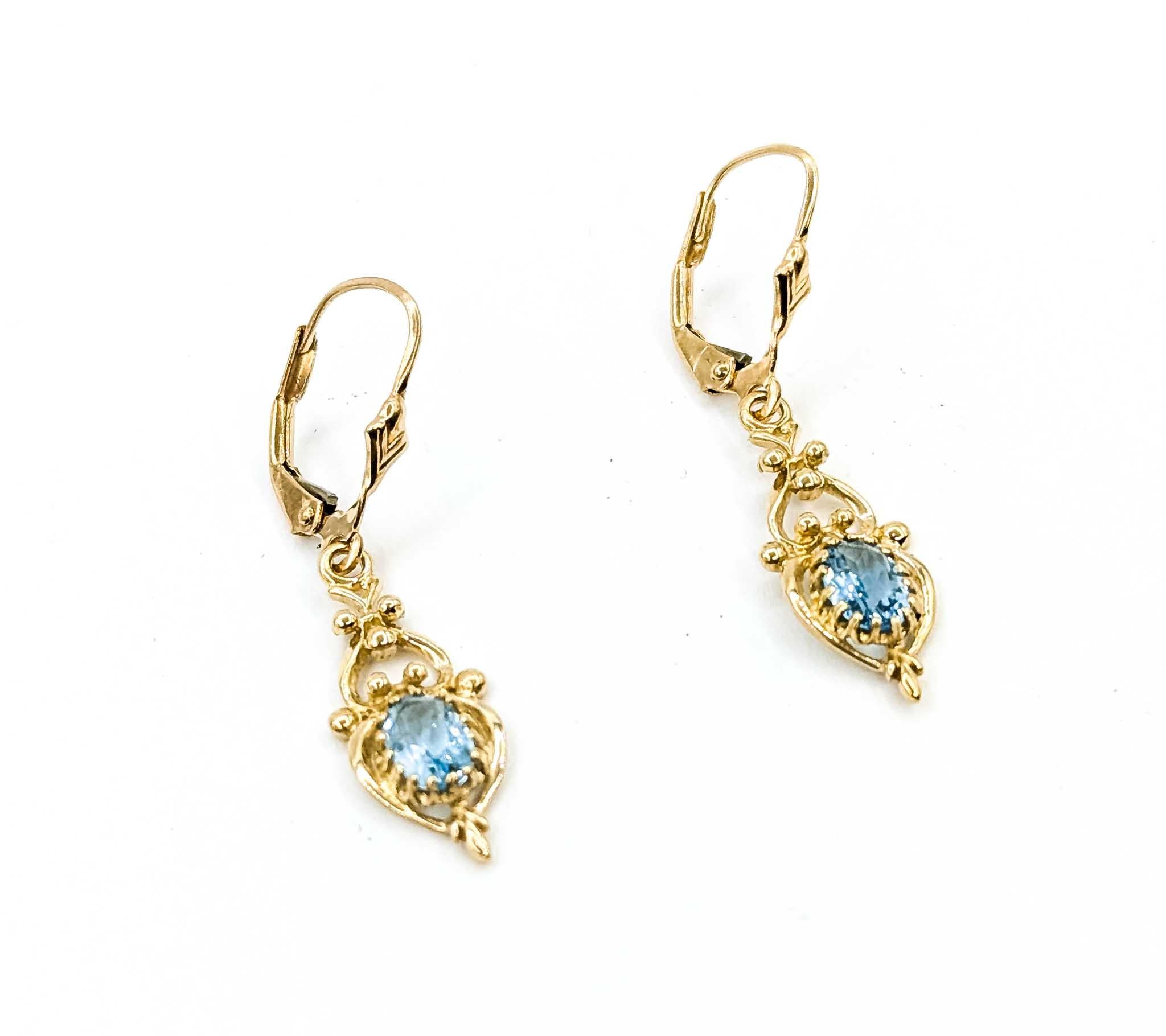 Estos elegantes pendientes colgantes están elaborados en oro amarillo de 10 quilates y engastados con gemas de topacio azul cielo de talla ovalada que suman aproximadamente 1,10 quilates. Las piedras están enmarcadas en ornamentados diseños calados