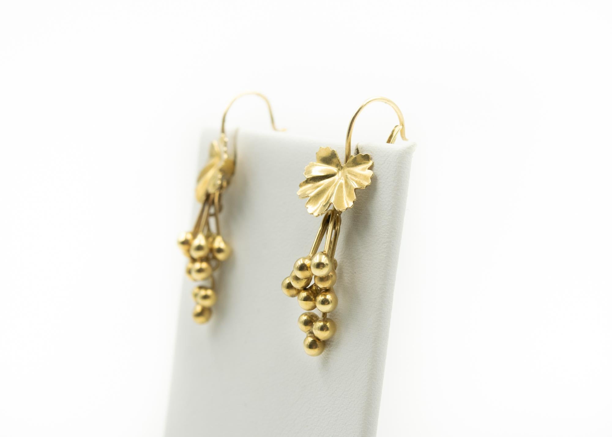 20th Century dangling drop earrings featuring a gold wire that leads to a fluted gold leaf with little balls that dangle at different lengths.  The dangling balls resemble grapes.  The earrings are marked 585 Italy for 14k.  The earrings have