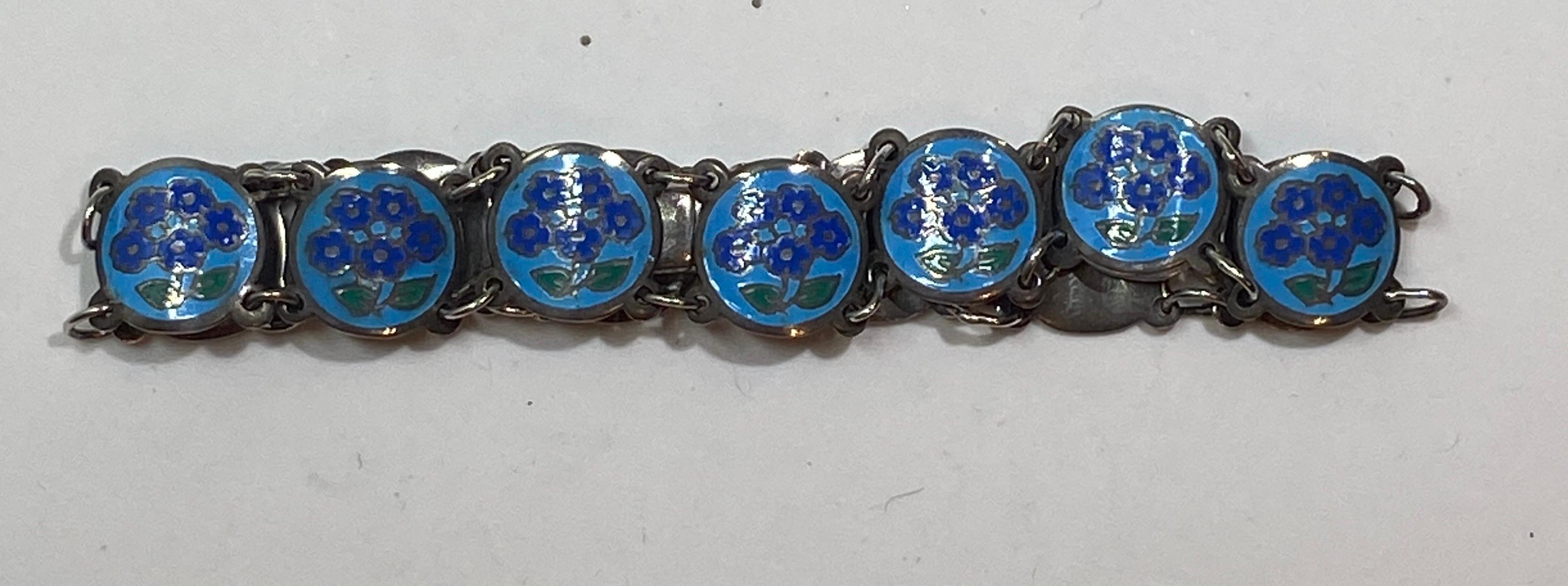 This delicate sterling silver link bracelet is detailed with multi-color floral enamel in shades of blues and greens. The length measures 6 1/2 inches. Width is 3/8 inch. On the opening clasp is etched with maker's mark. Made in Thailand.