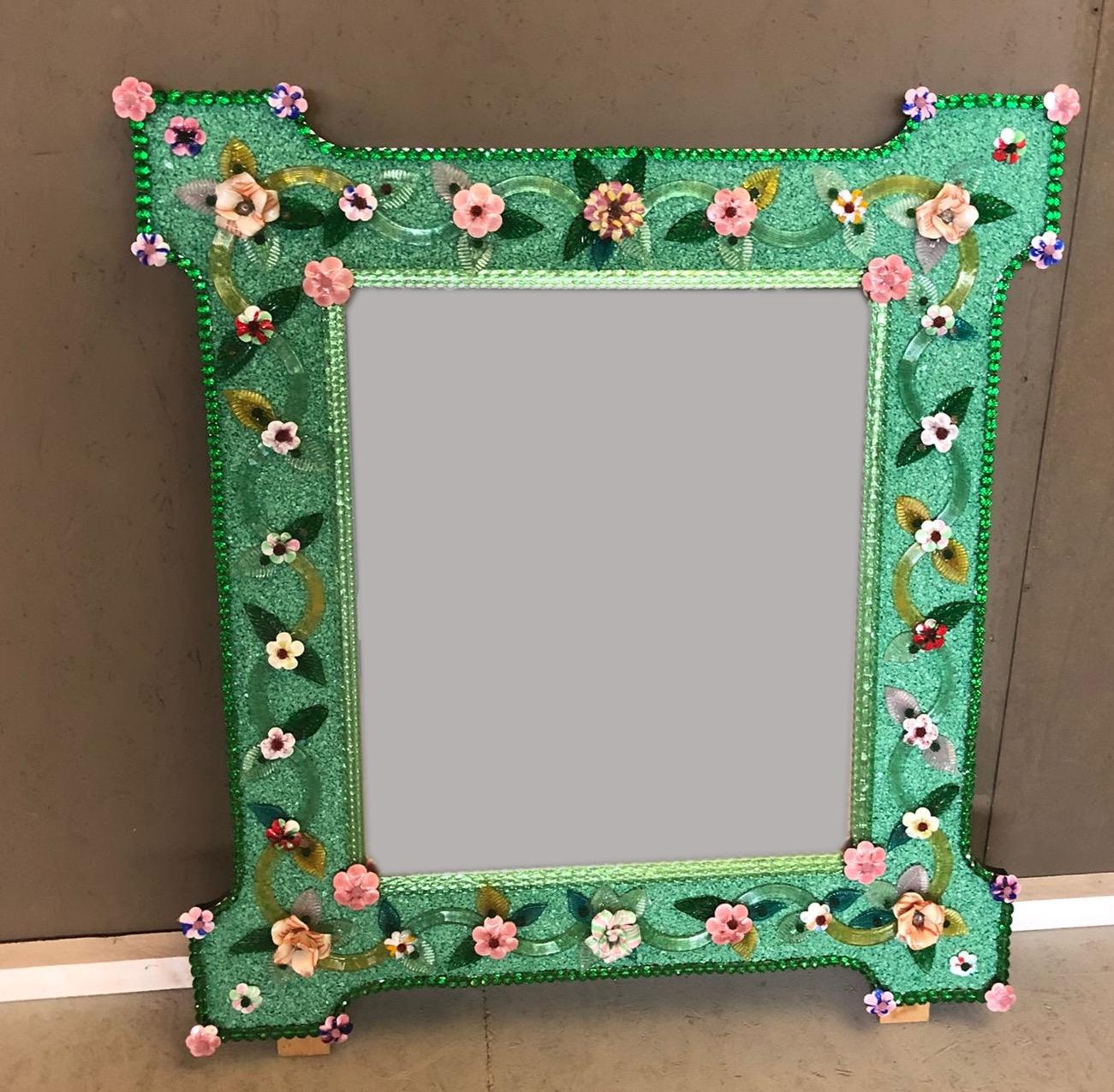 Charmant miroir vénitien avec cadre vert. Le long des bords du cadre se trouvent des accents de corde en verre vert et de nombreuses fleurs multicolores en verre pasta vitrea.
Exécuté par le grand maître de Murano.
Excellent état.
  