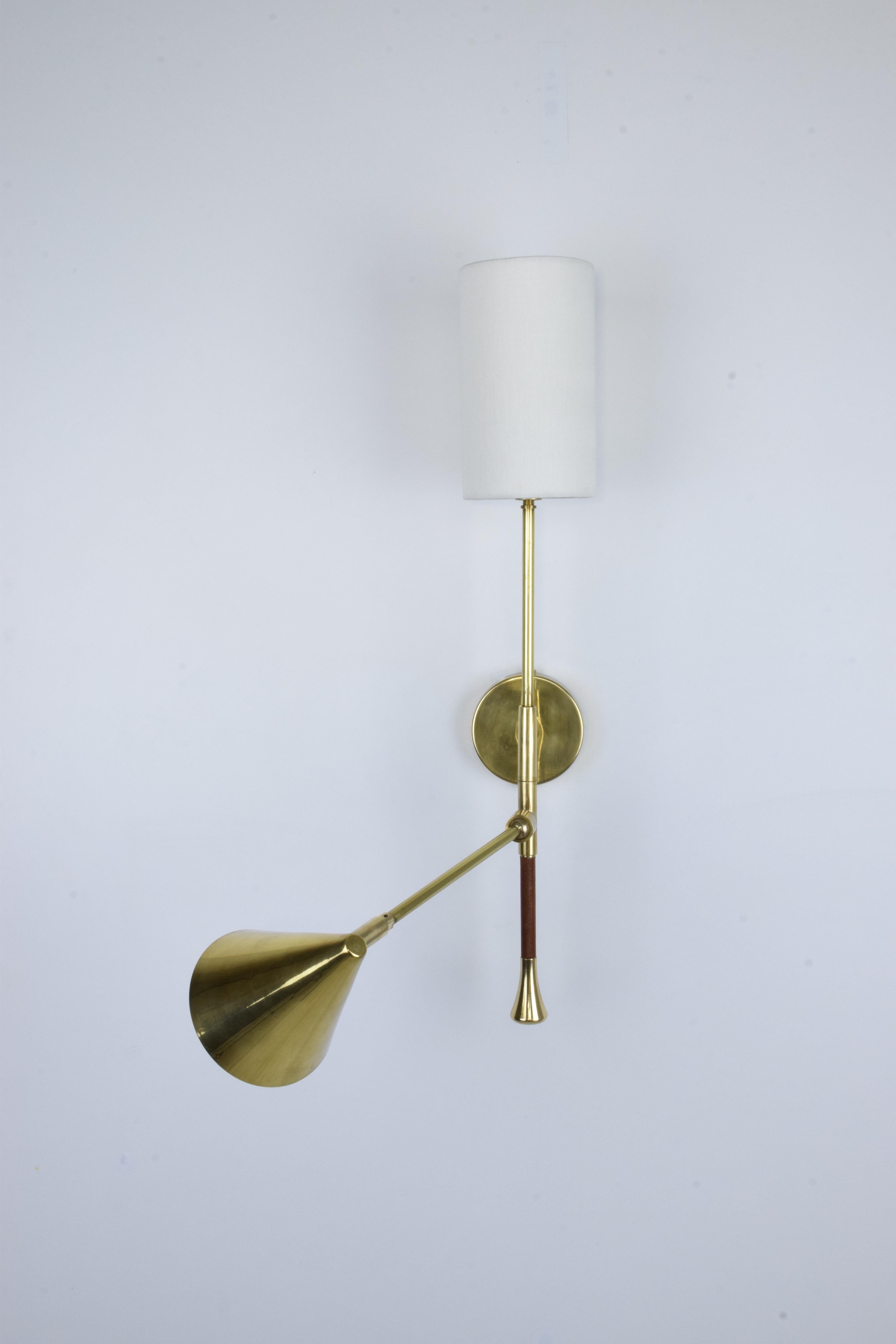 The DE.LIGHT is a solid brass double wall light with a leather sheathed stem detail. The main structure tops a cylinder fabric shade or an opal glass di user and the directional stem features a conic shade mounted with a moveable joint. Perfect as a