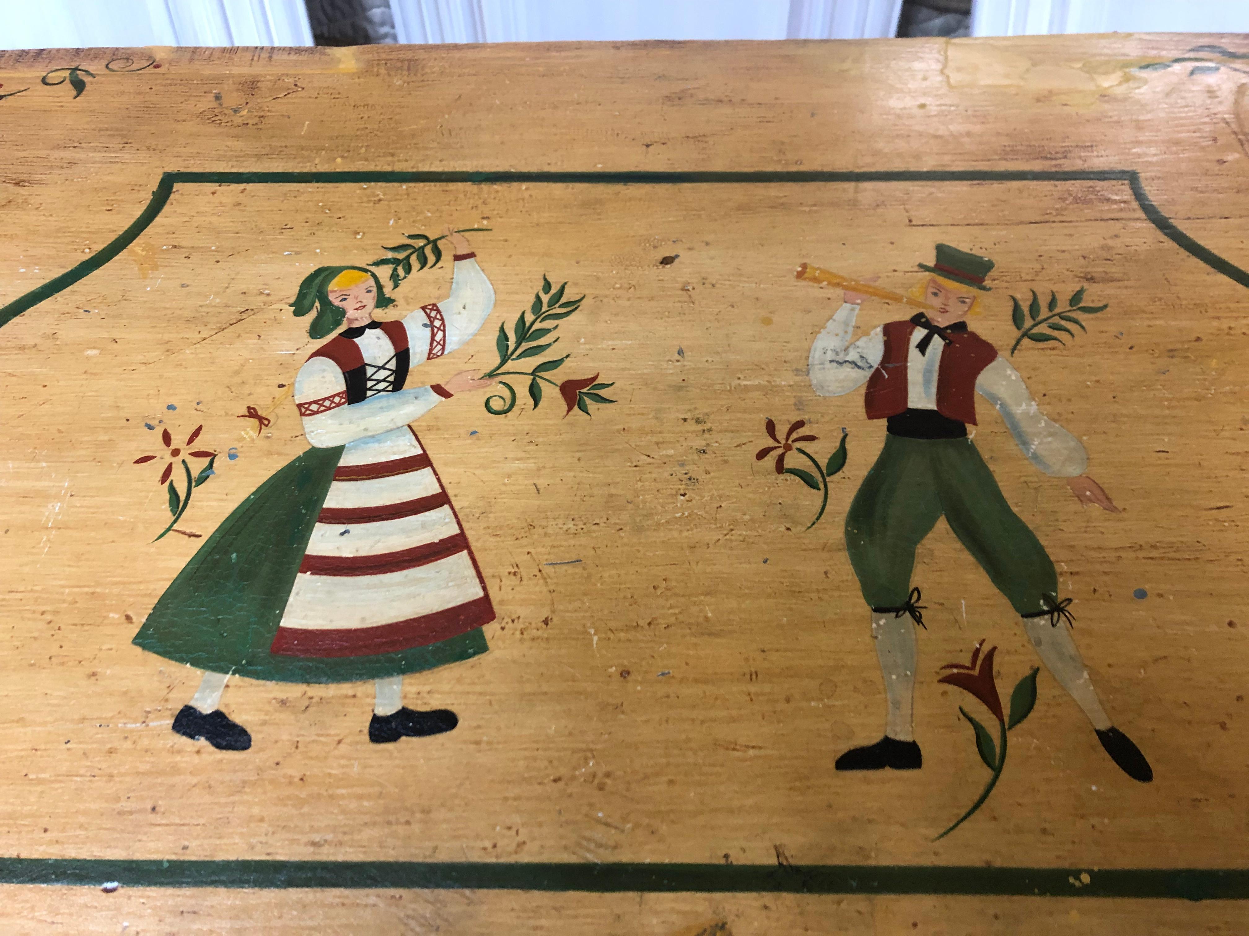 A wonderful folk art hand painted antique trunk or chest in a yellow gold having charming male and female Dutch peasants adorning the top. Great size for a small coffee table with storage or at the end of a bed.