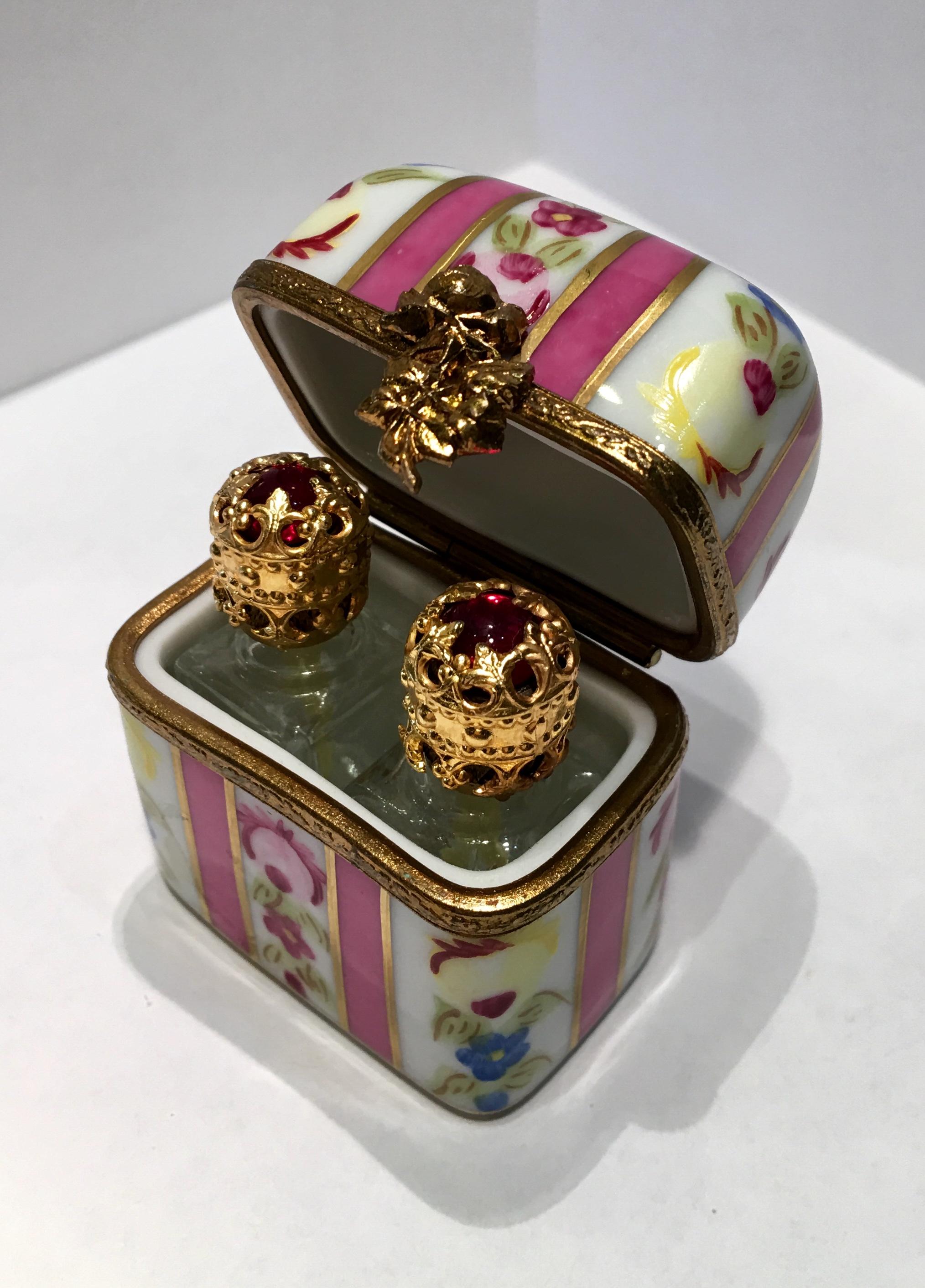 Exquisitely handmade and hand painted vintage miniature Limoges porcelain box with a hinged lid is decorated with flowers and features lavish stripes of 24-karat gold outlining wide pink stripes. The porcelain box and lid feature rims or fittings of